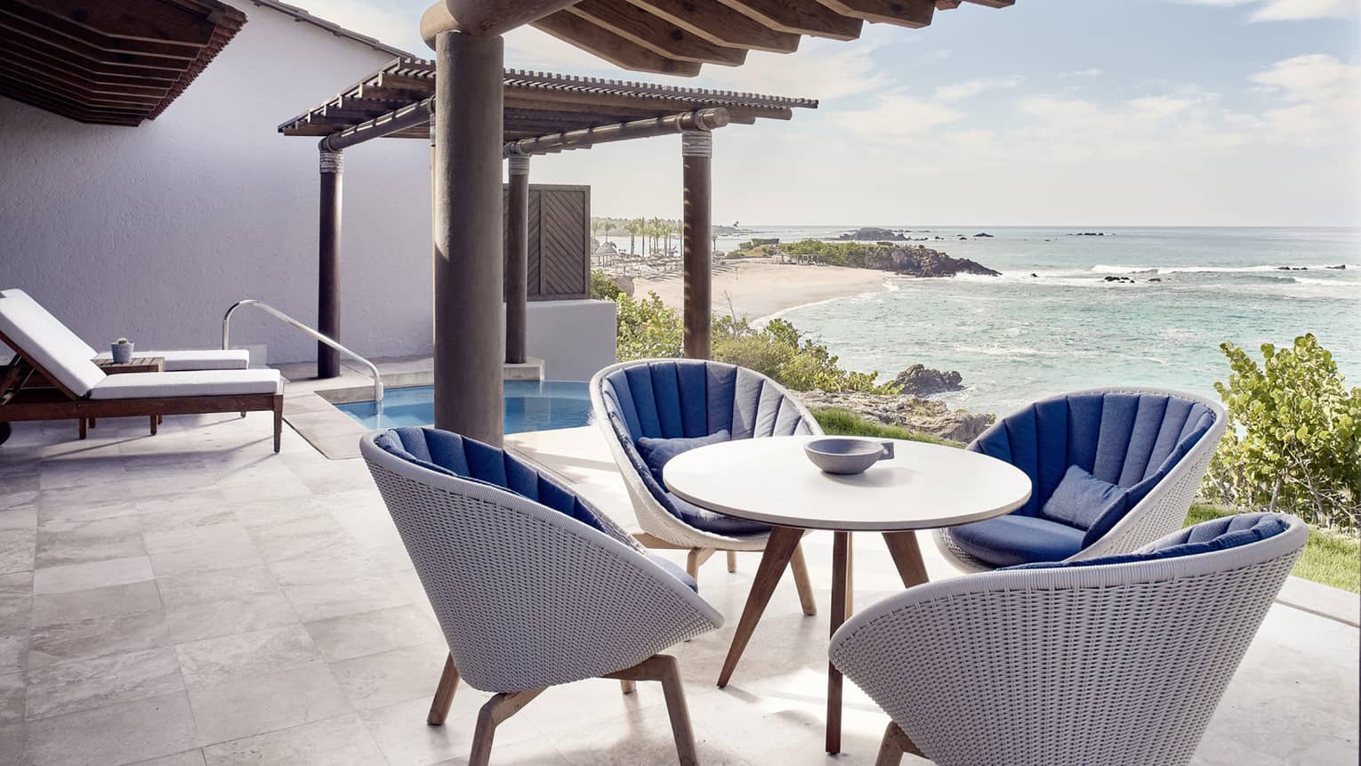 The private outdoor terrace of a modern suite near Puerto Vallarta, with ocean view and plunge pool, featuring a table and four white wicker chairs