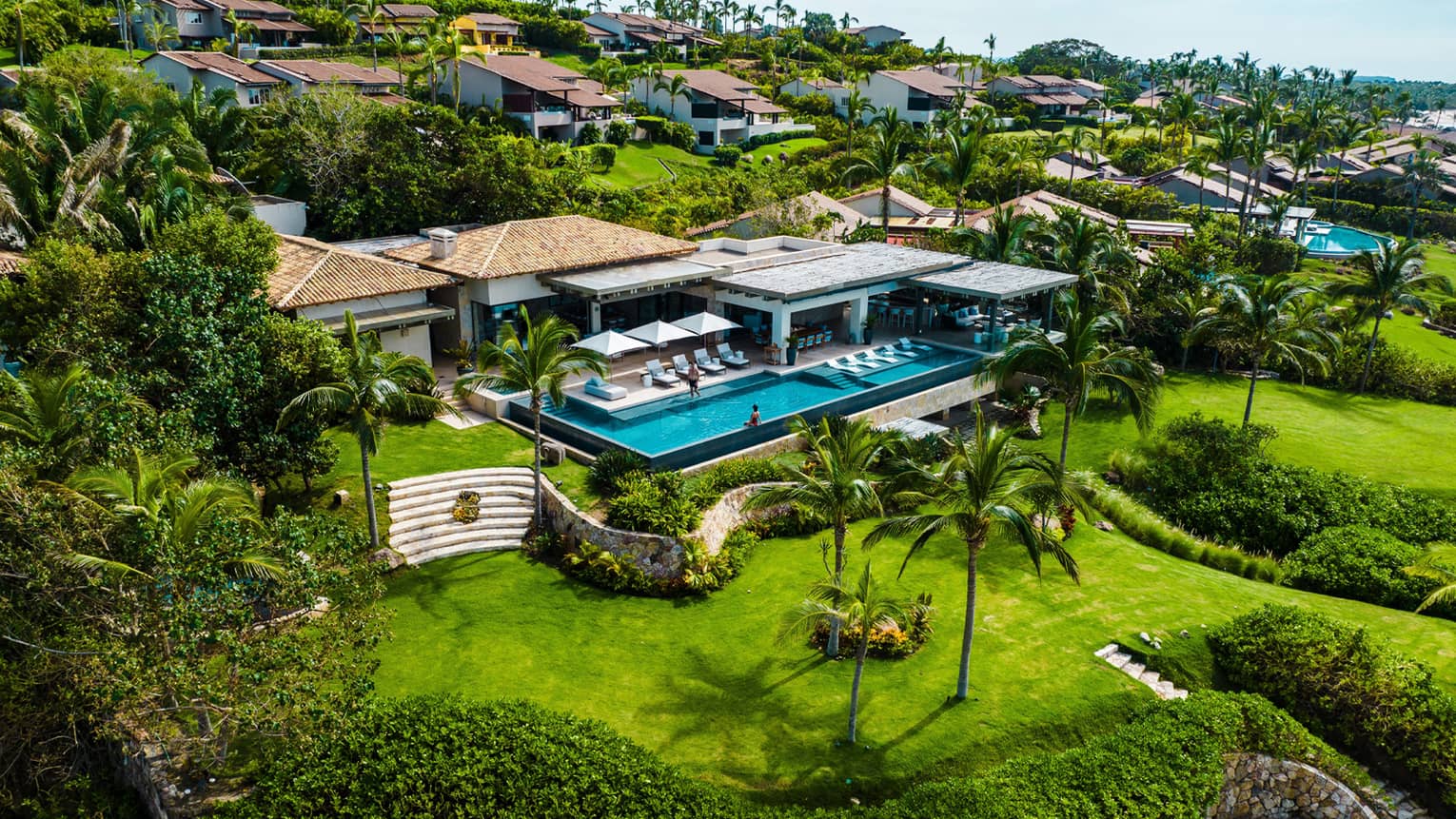 Luxury villa with large rectangular infinity pool and lush green landscaping by the ocean
