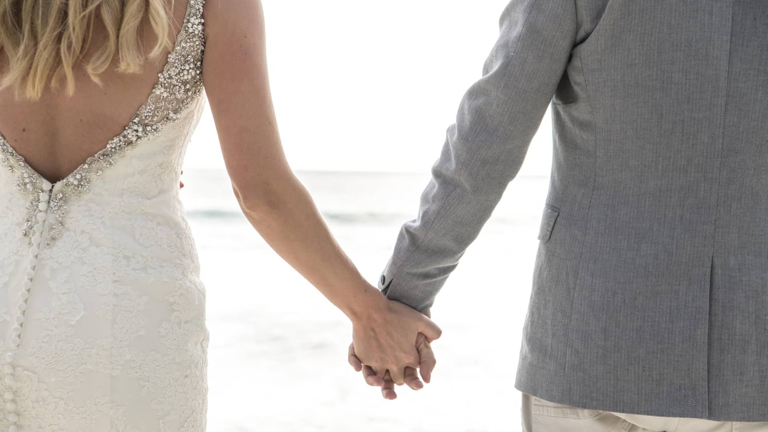 Bride and groom holding hands and facing ocean