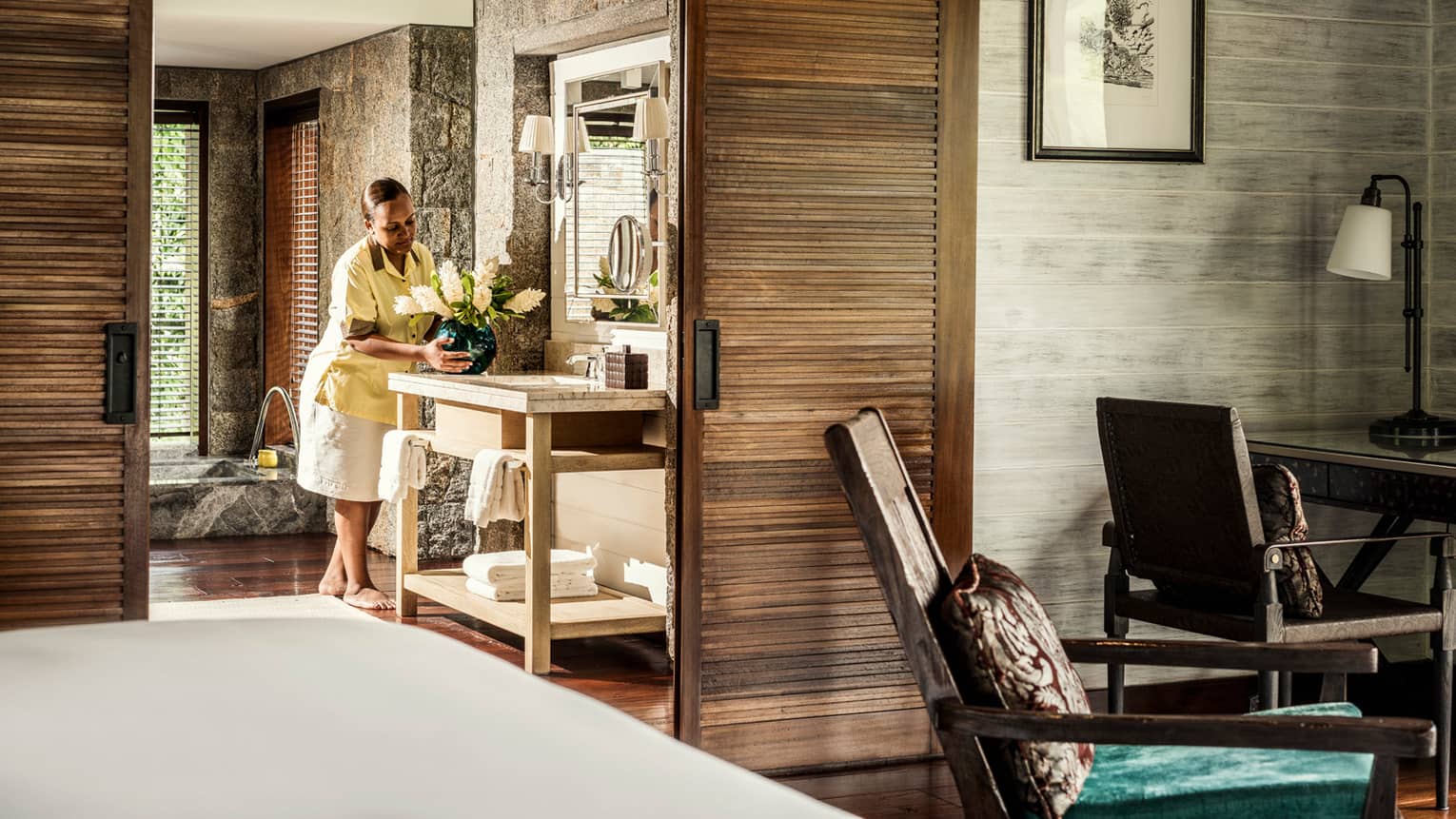 Villa butler places vase of flowers on vanity with towels in large bathroom