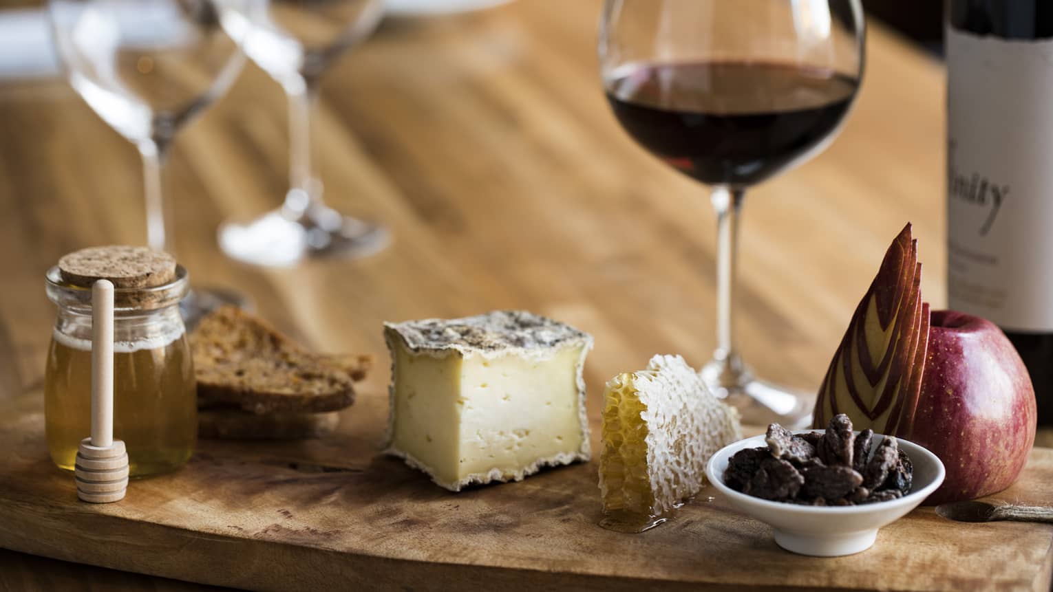 Red wine, cheeses and small jar of honey on cheese board