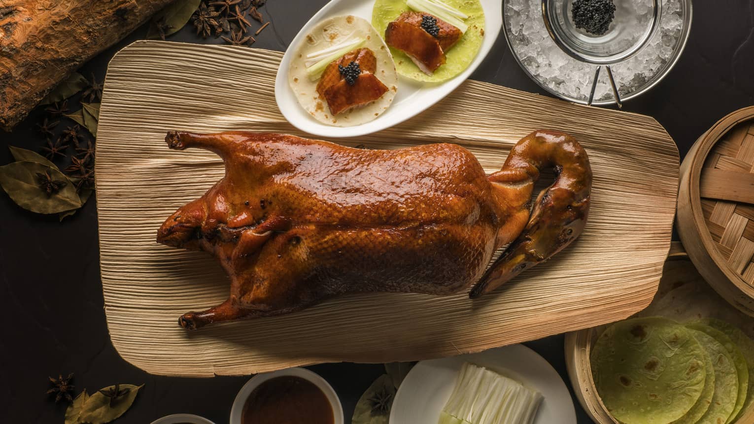 Aerial view of whole Peking duck on wood platter beside small dishes with slices