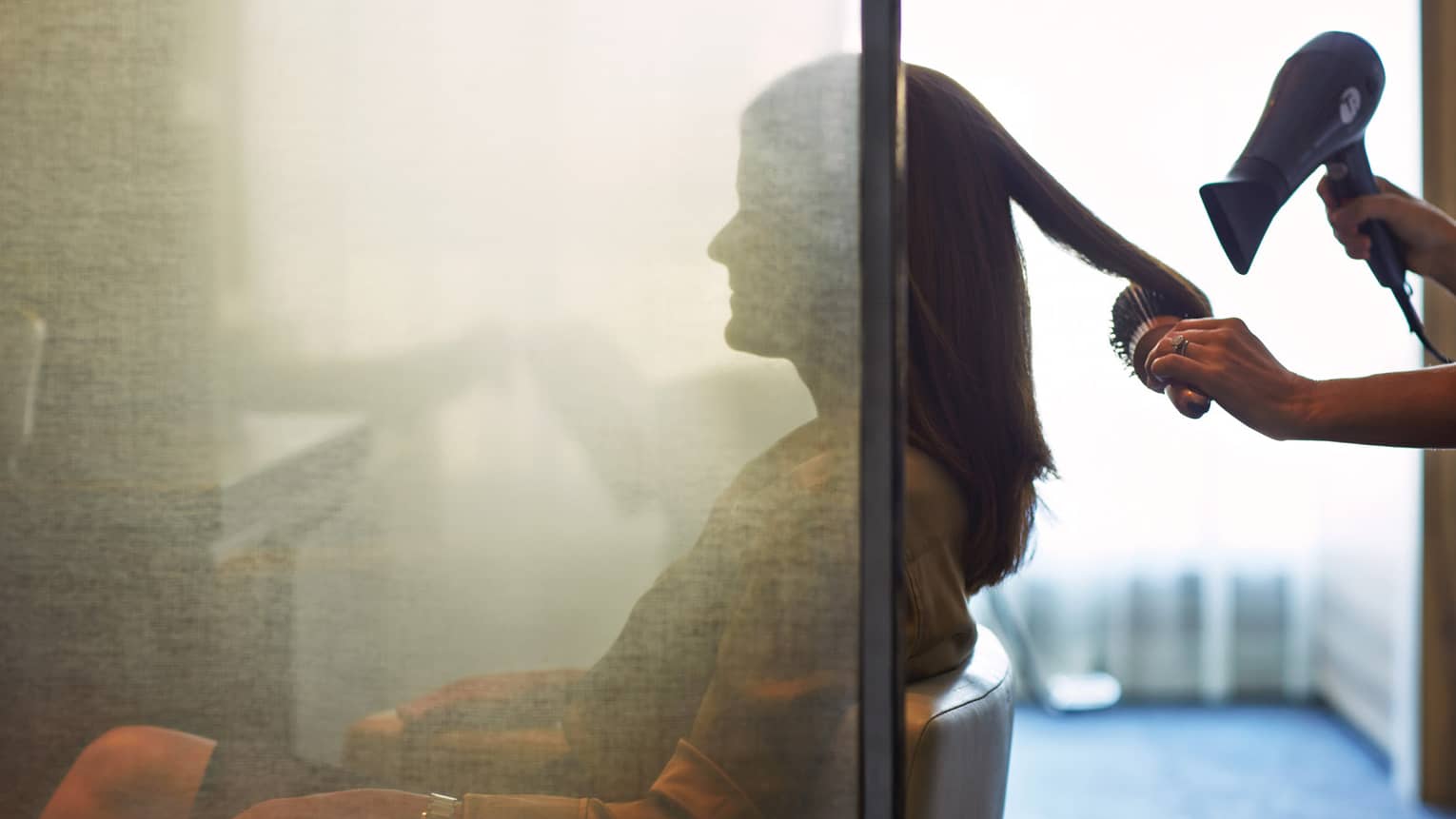 Silhouette of woman behind salon screen as hair stylist brushes and blow-dries hair