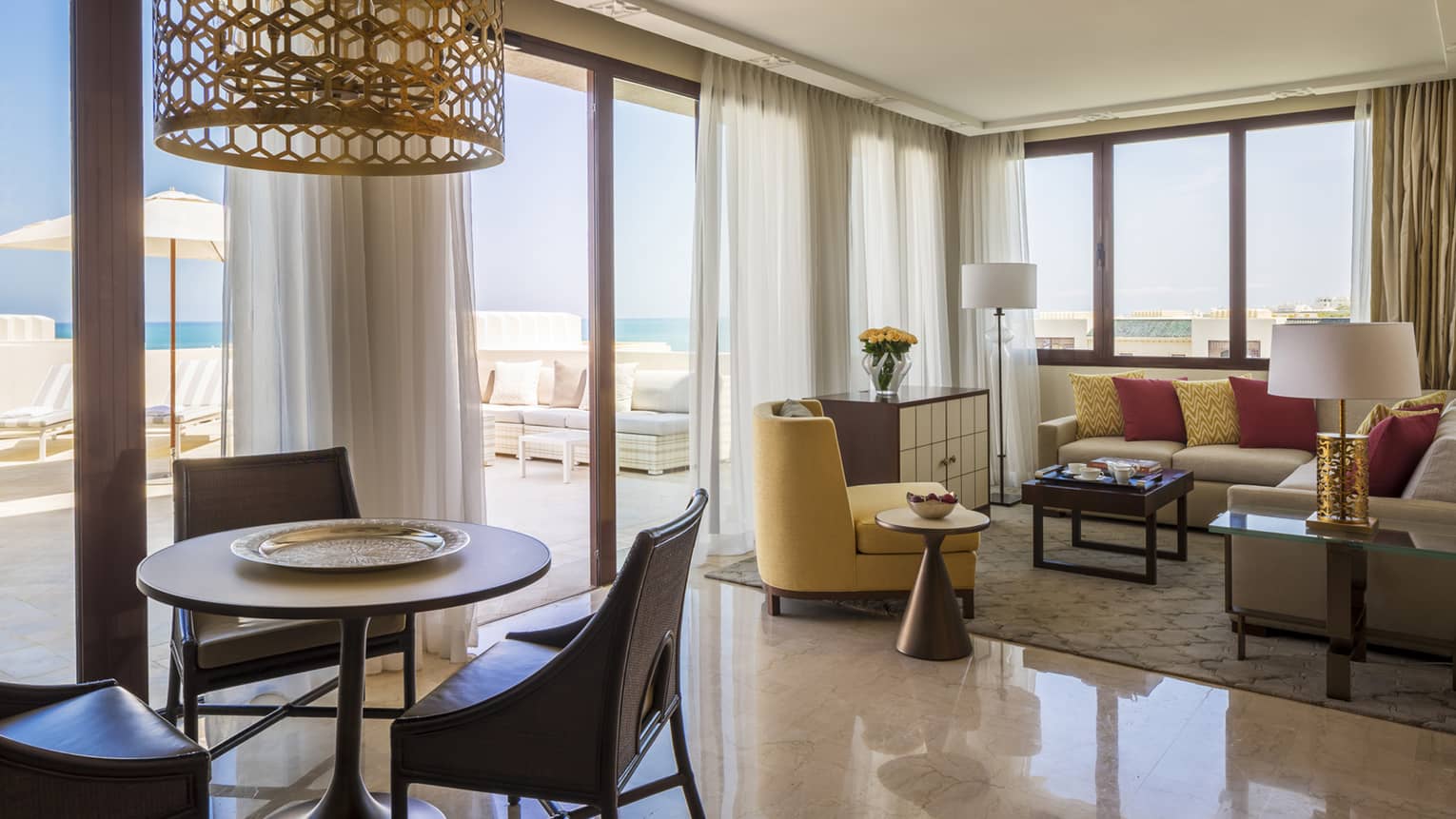 Living room with mustard-coloured chair and sofa, connecting to dining area with round table and three chairs, chandelier
