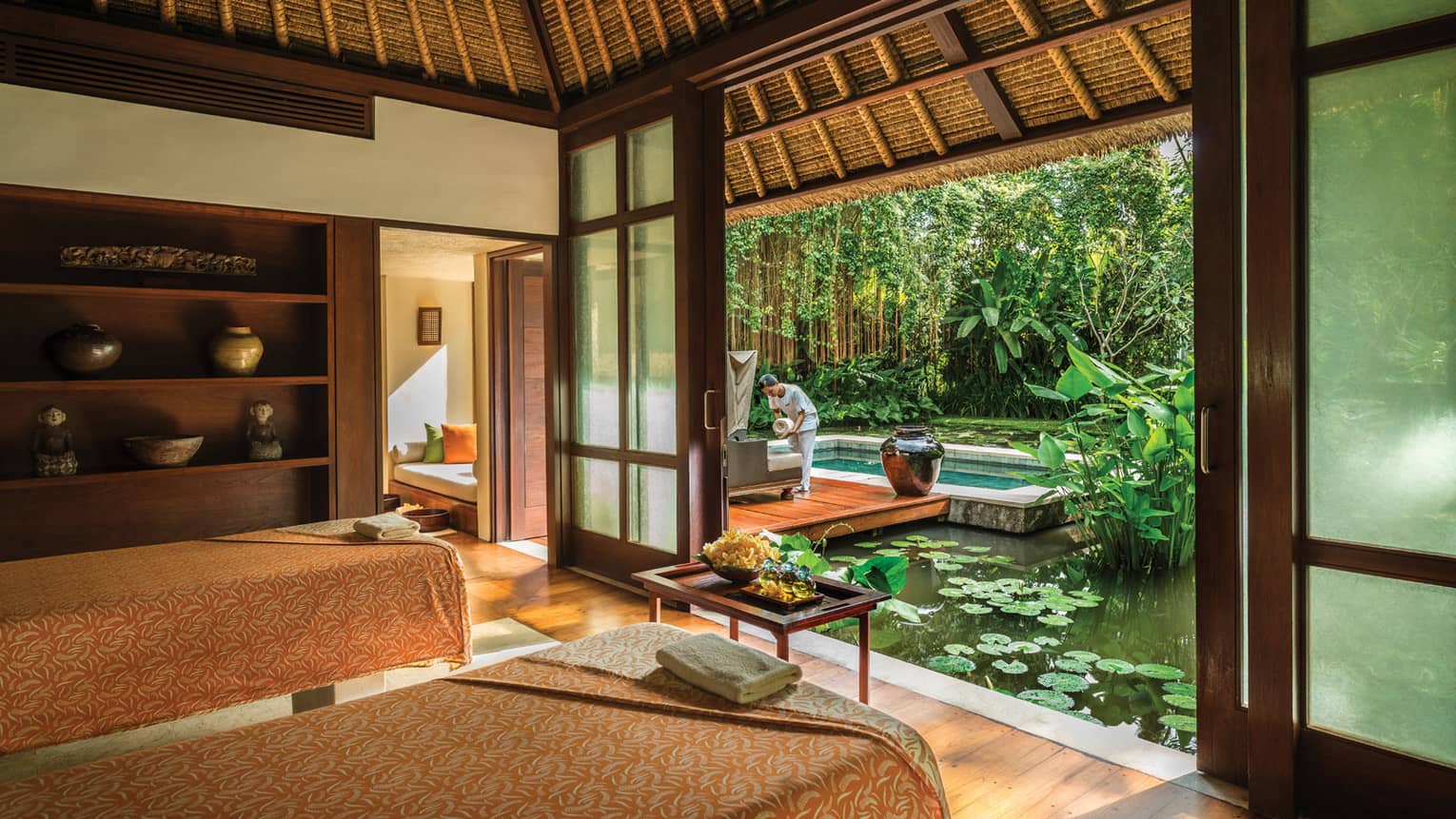 Two massage beds in spa room with door open to lily pond where spa attendant sets down rolled white towel