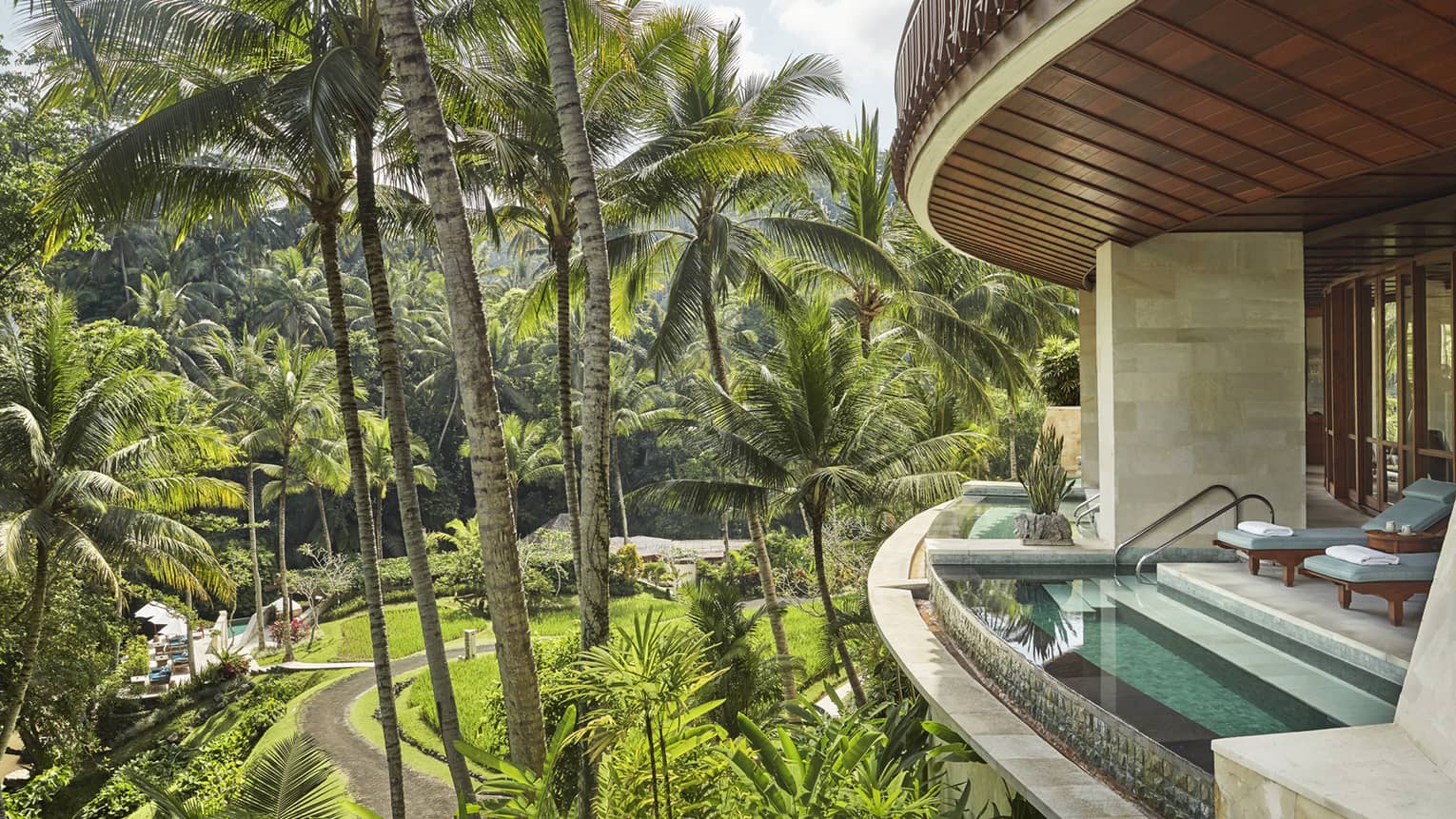 Curved private balcony with plunge pool at edge of terrace, blue lounge chairs, sunny garden far below