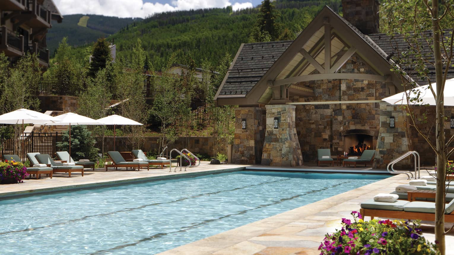 Year-round outdoor pool with brick patio and chalet-style cabana with fireplace and lounge chairs