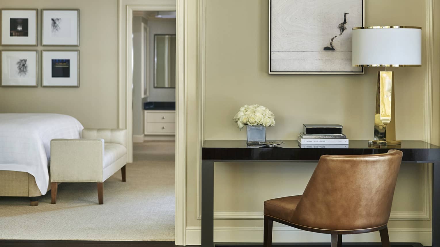 Modern brown leather office chair at black desk by doorway leading to bedroom, bed and bench visible