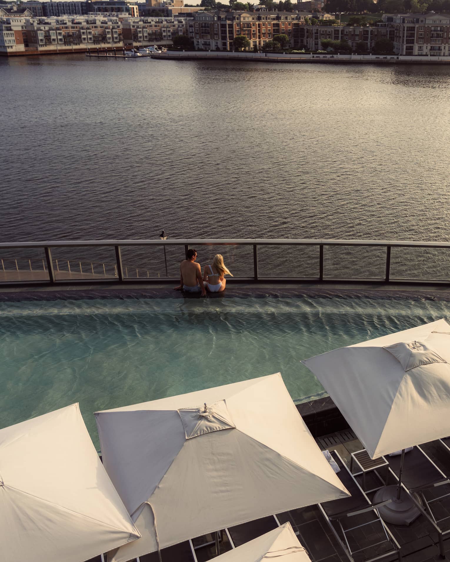 Two people sitting on the edge of a pool overlooking the harbour.