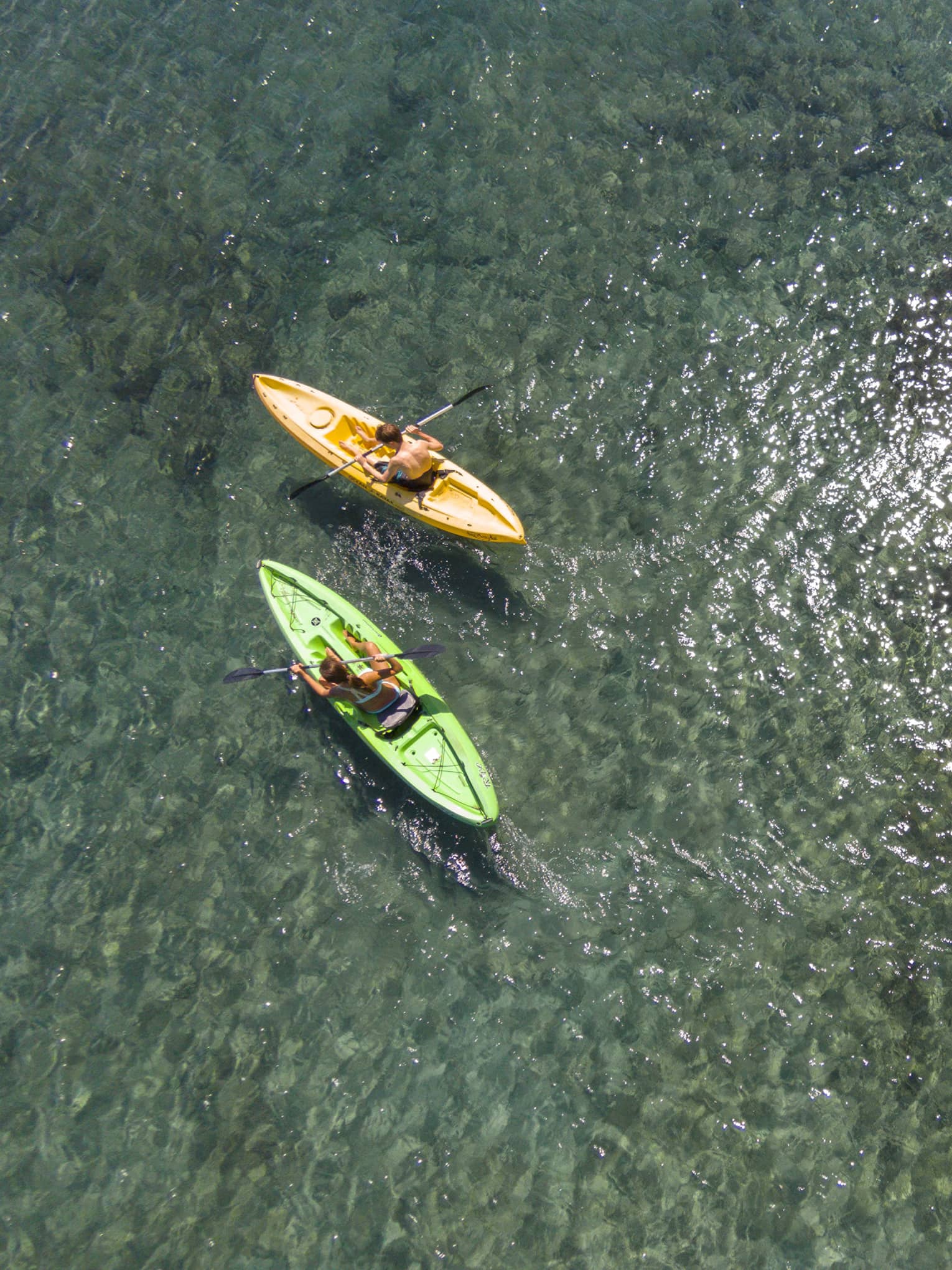 Aerial view of man and woman in green and orange kayaks on reef