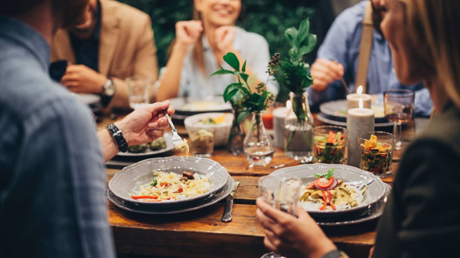Close-up of group of friends around gourmet pasta dishes on outdoor table