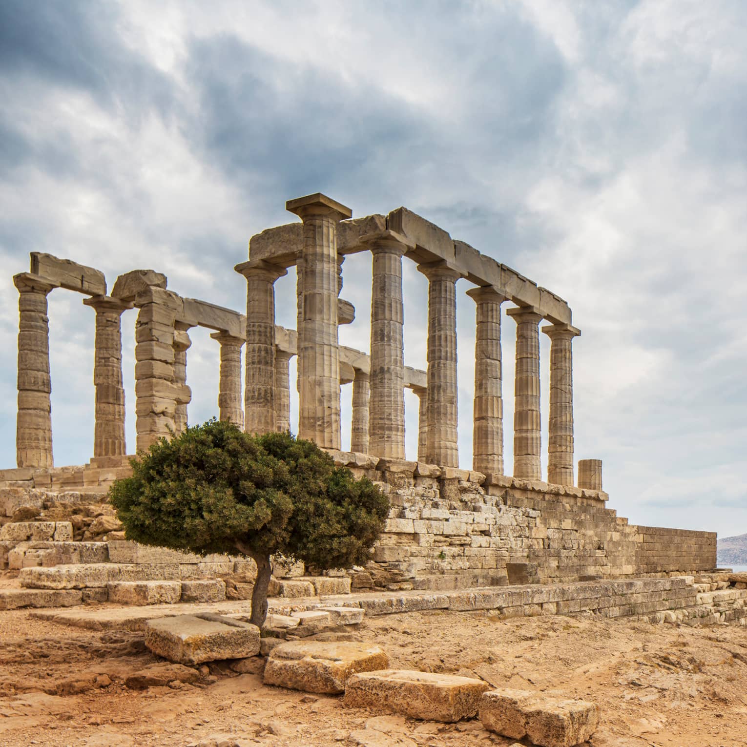 Ancient ruins stand near water under sky with clouds