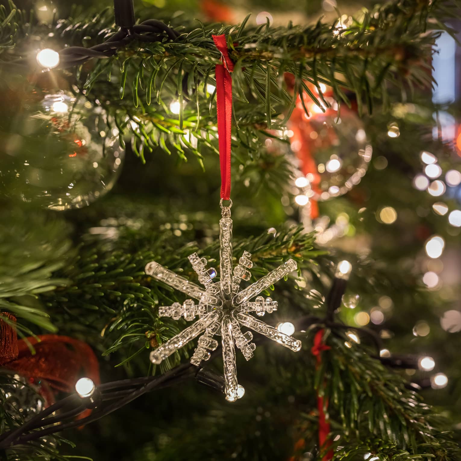 Close-up of a crystal snowflake ornament hanging on a Christmas tree with festive lights in the background