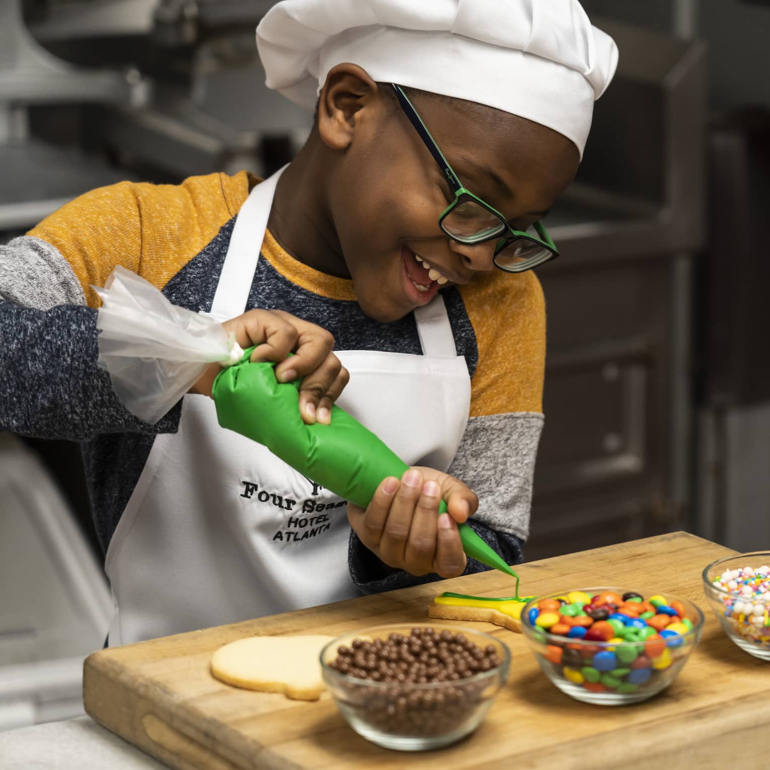 A child in an apron and chefs hat decorating sugar cookies with icing and candy.