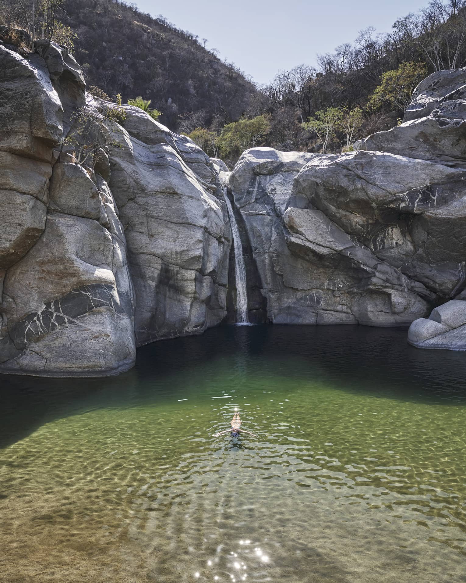 A person in a small well of water surrounded by large rock faces and trees.