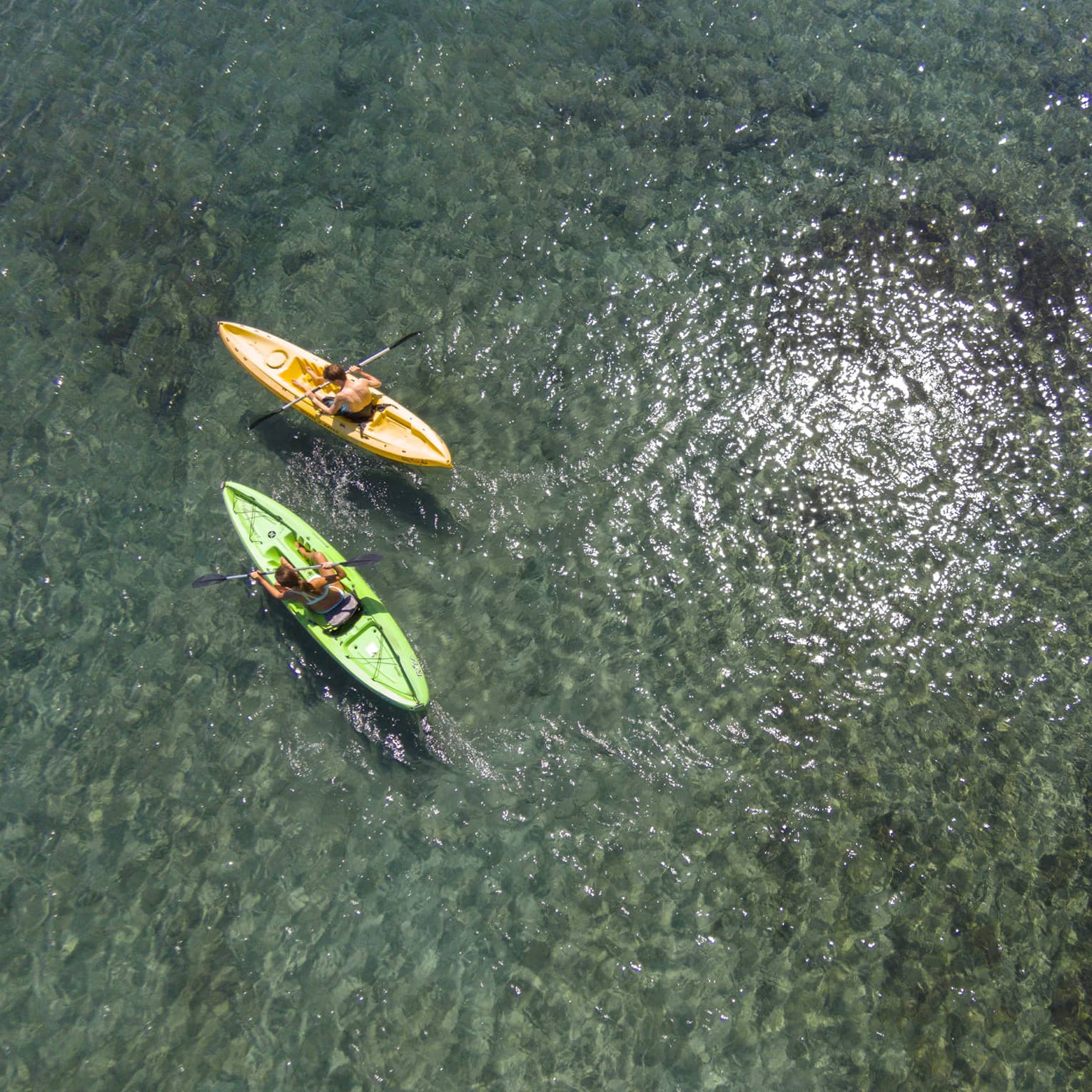 Aerial view of man and woman in green and orange kayaks on reef