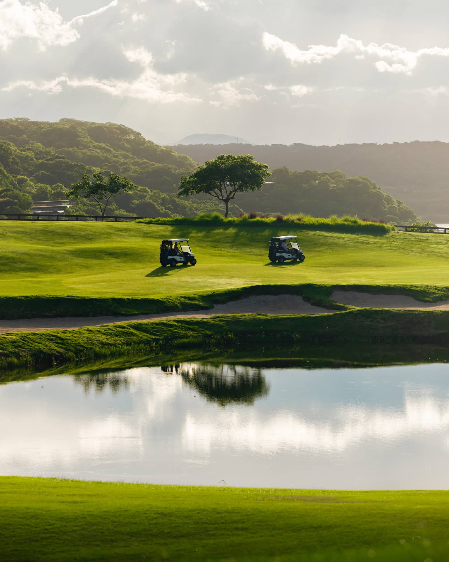 Two golf carts drive along a course next to a water feature