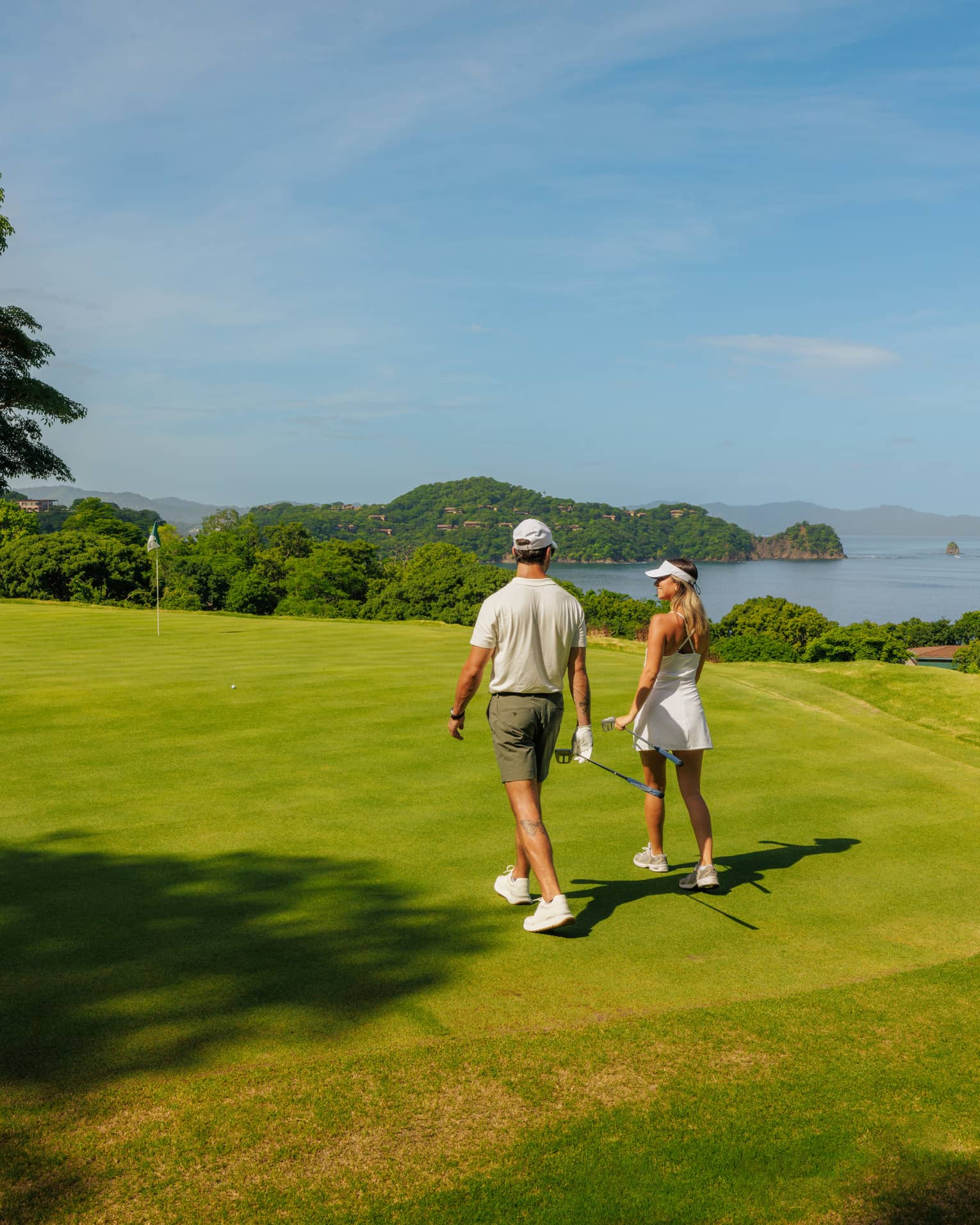 Two golfers walk side by side along a greenway with the ocean in the background