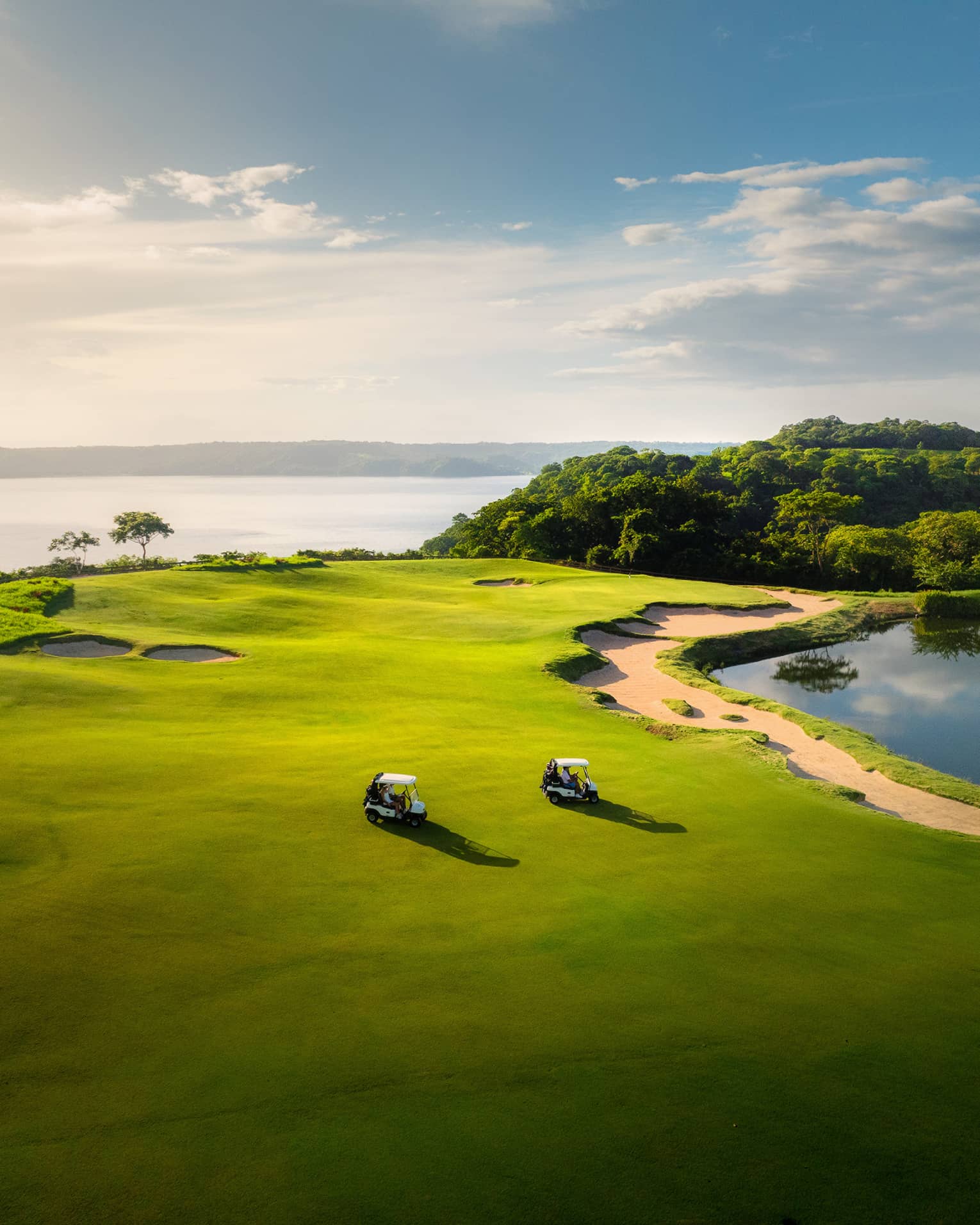 Two golf carts ride along a green with the ocean in the background