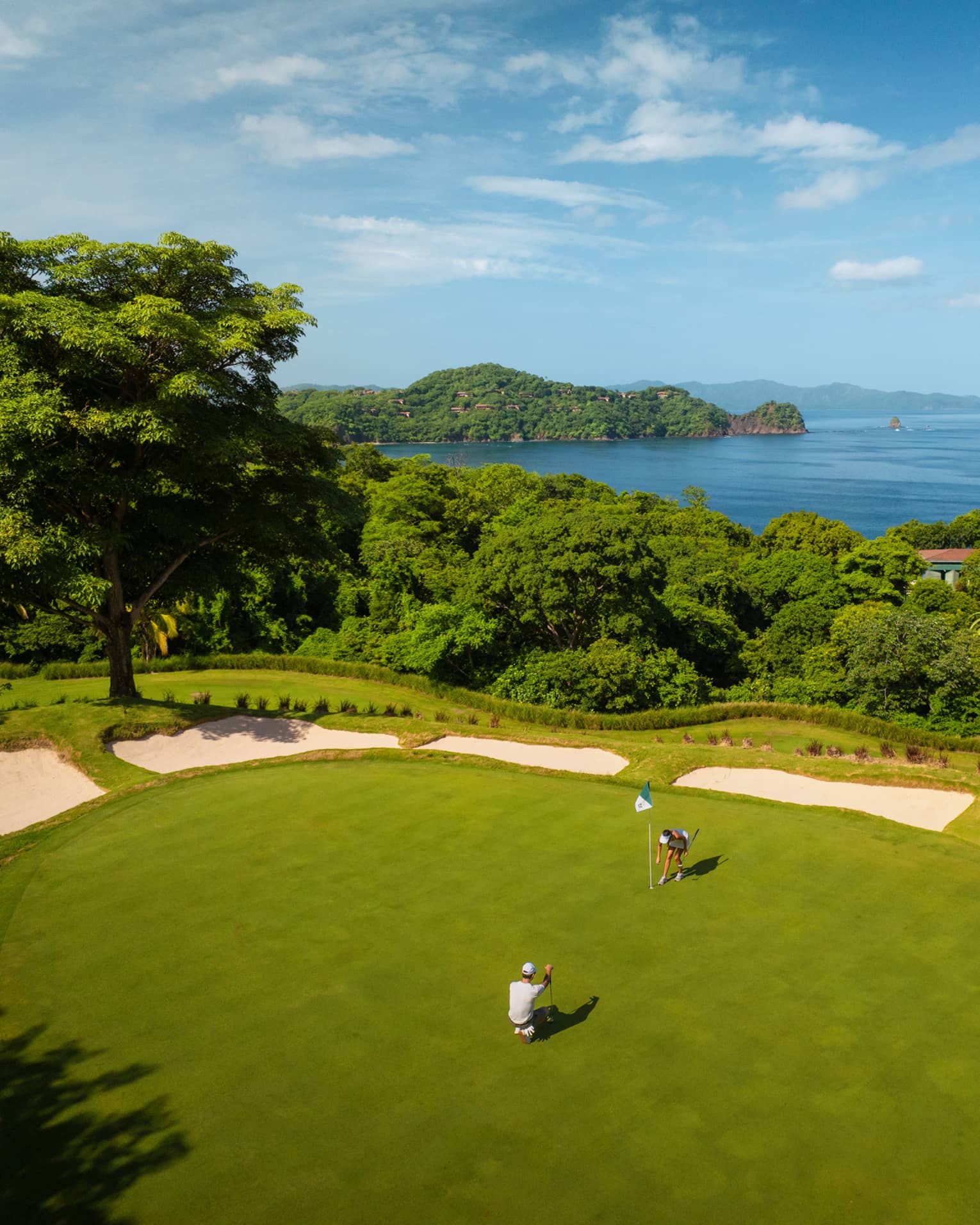 Aerial view of two golfers on a green with the ocean in the background