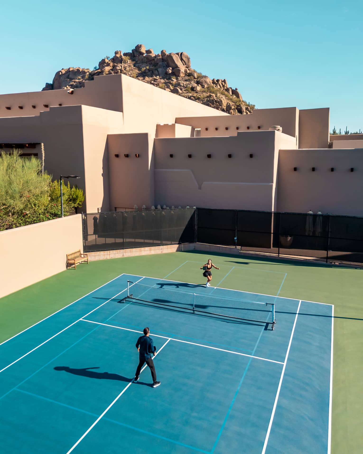 Aerial view of two guests playing a game of tennis.