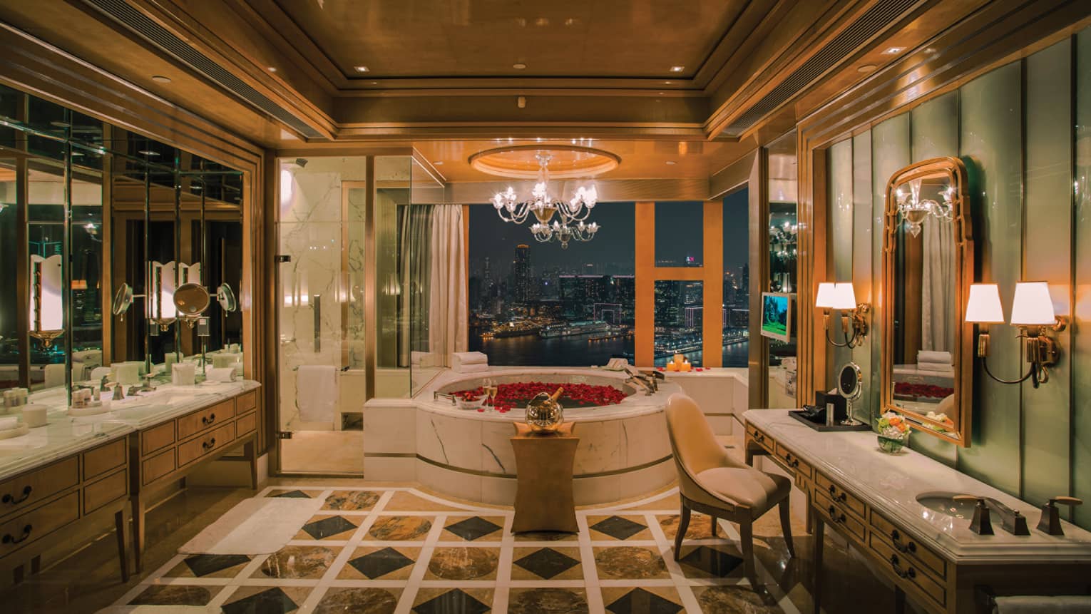 Large candle-lit hotel room bathroom with circular spa tub filled with red rose petals