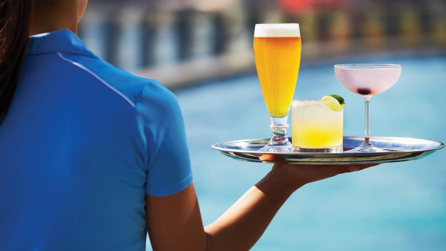 Close-up of woman wearing blue uniform holding tray with beer pint, cocktail, pink martini
