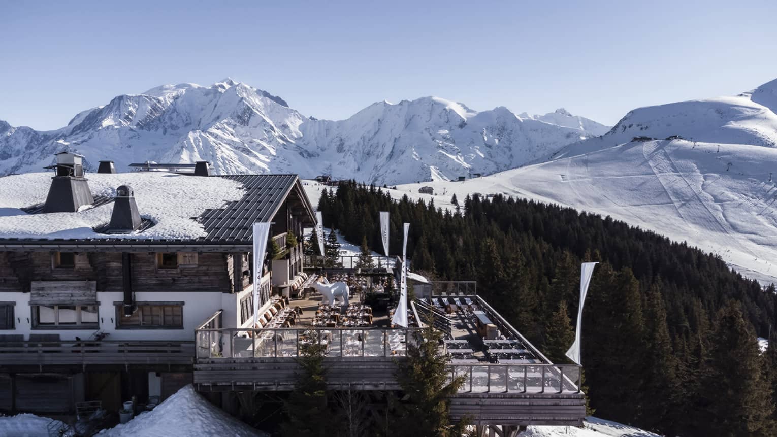 Large snow-covered chalet with expansive deck, surrounded by snow-covered mountains
