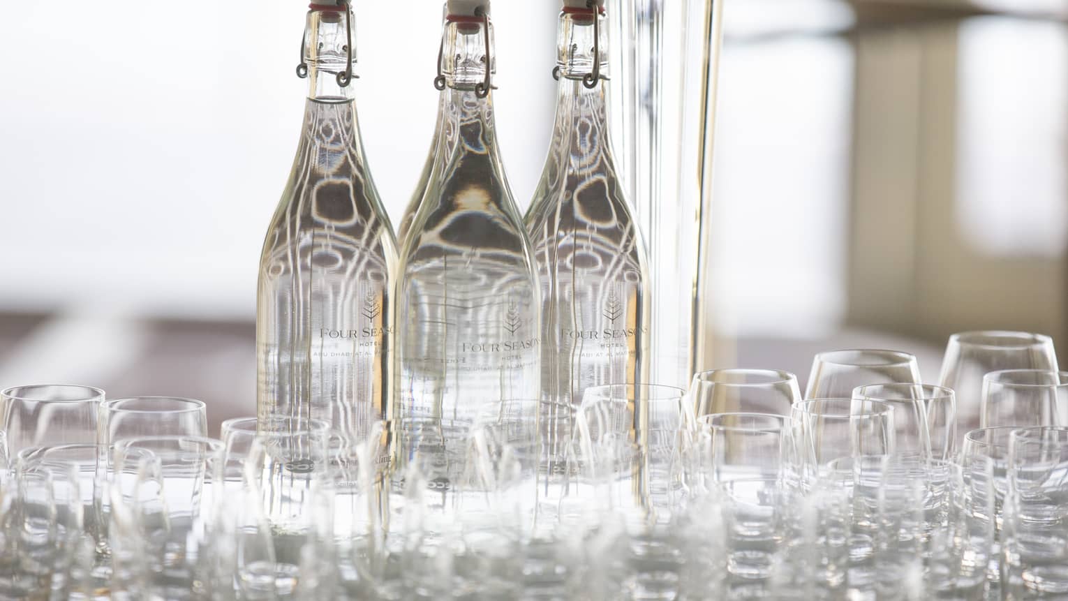 Close-up of water tray with rows of empty glasses, three large cork top glass bottles