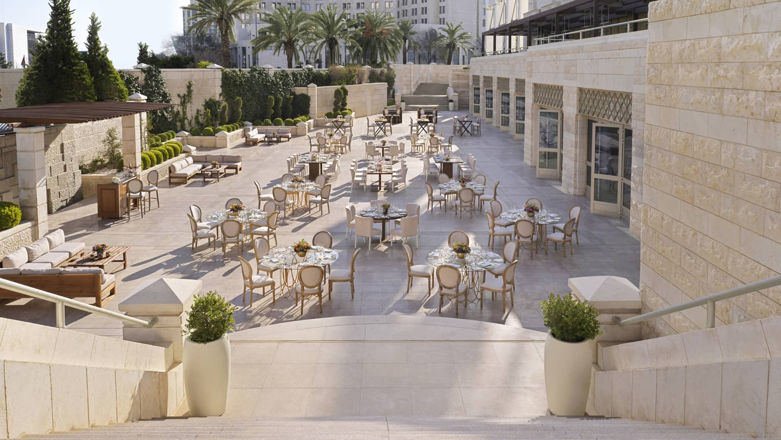 A shot of a descending staircase towards a series of gold chairs in front of white linen tables.