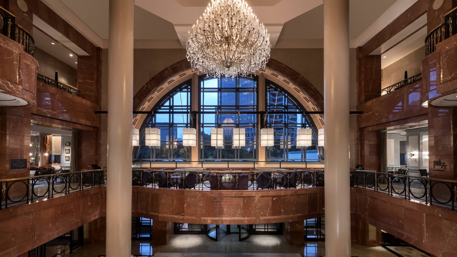 Large chandelier hangs between tall marble columns, floor balconies, in front of arched window