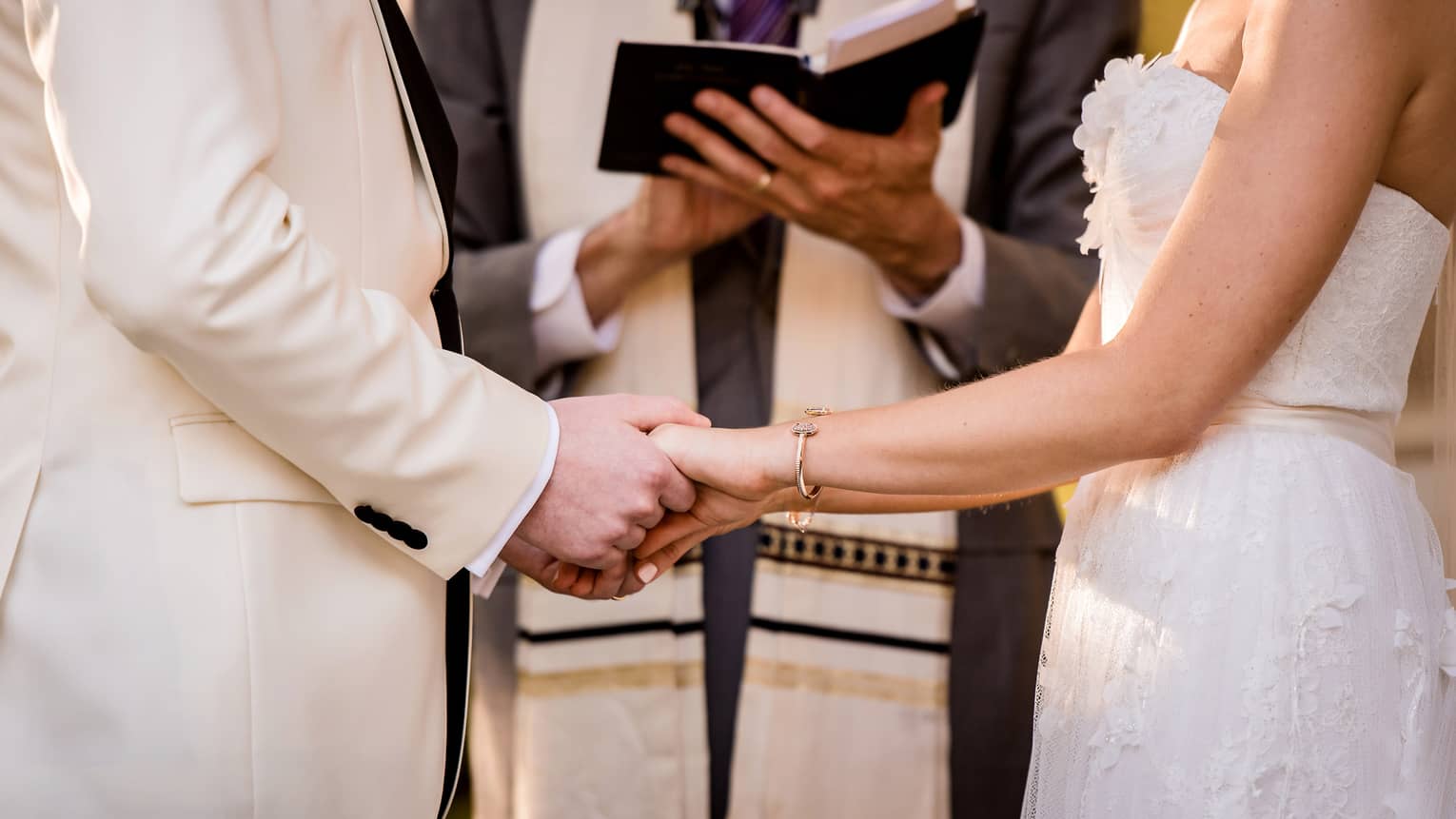 Bride and groom hold hands in front of wedding ceremony officiant