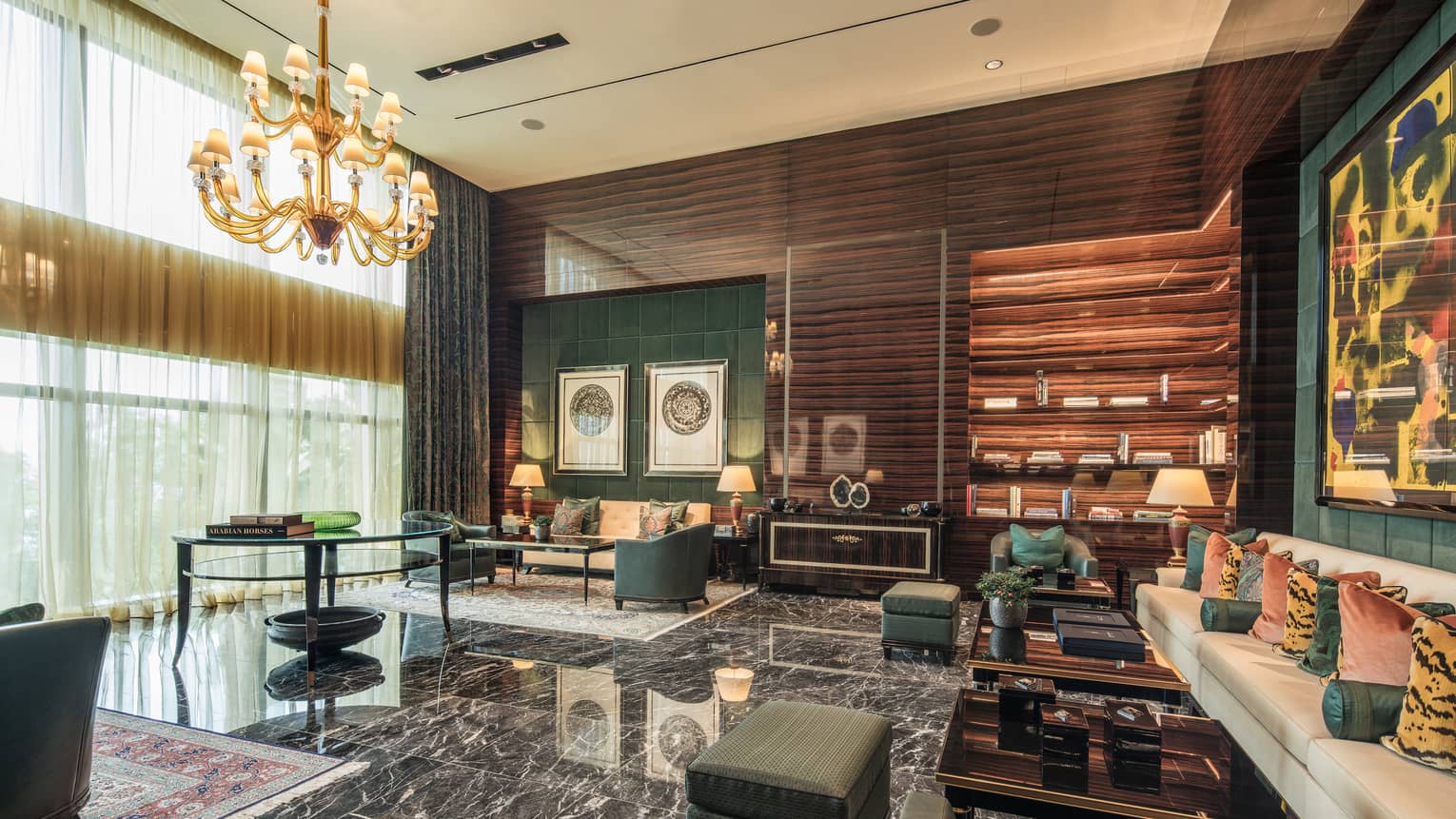 A room with a marble floor and several forest green and cream couches, all seated under a golden chandelier. 