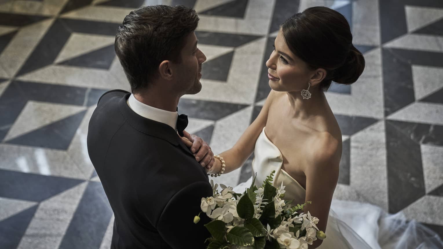 Groom and bride with white floral bouquet embrace in banquet room with black and white floors