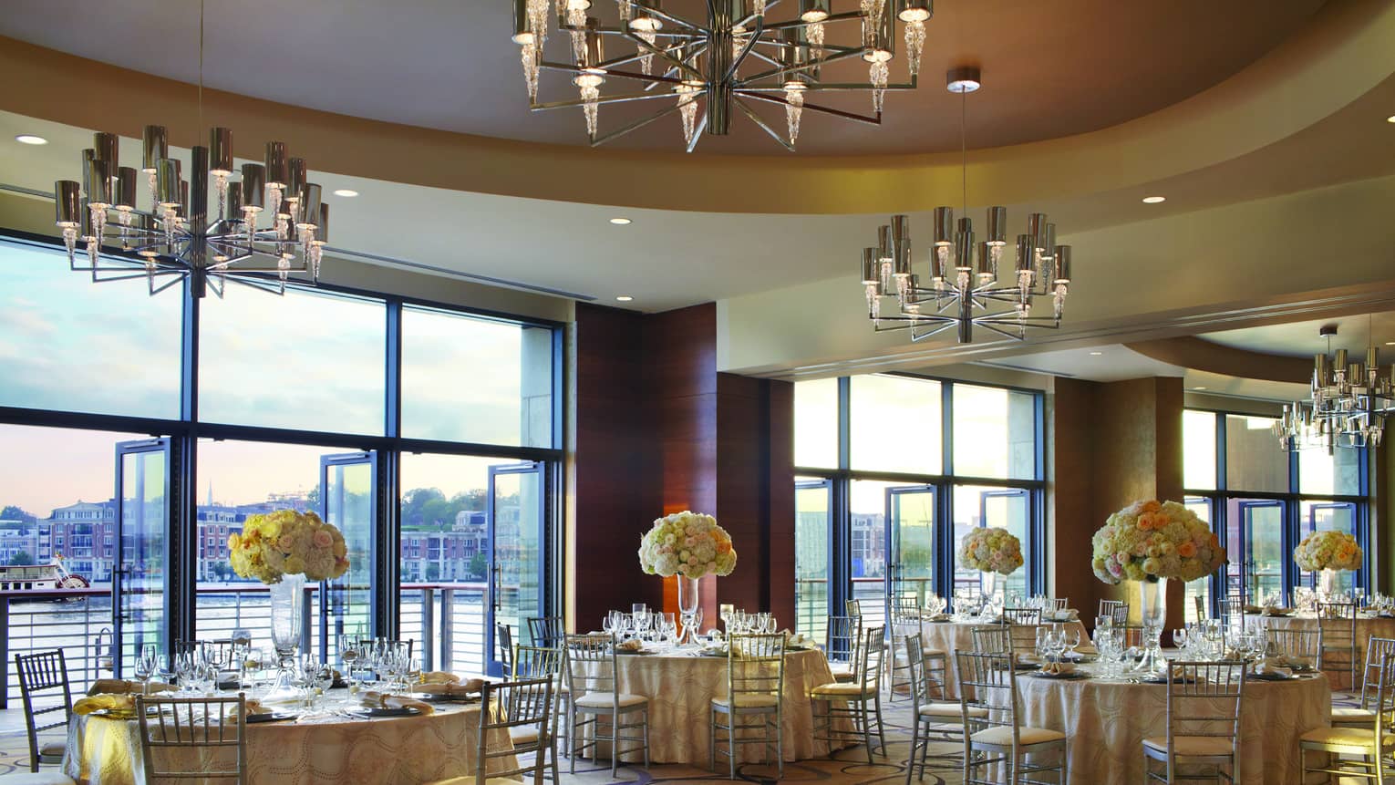 Ballroom with elegant round banquet tables by open air floor-to-ceiling windows overlooking Harbor East water