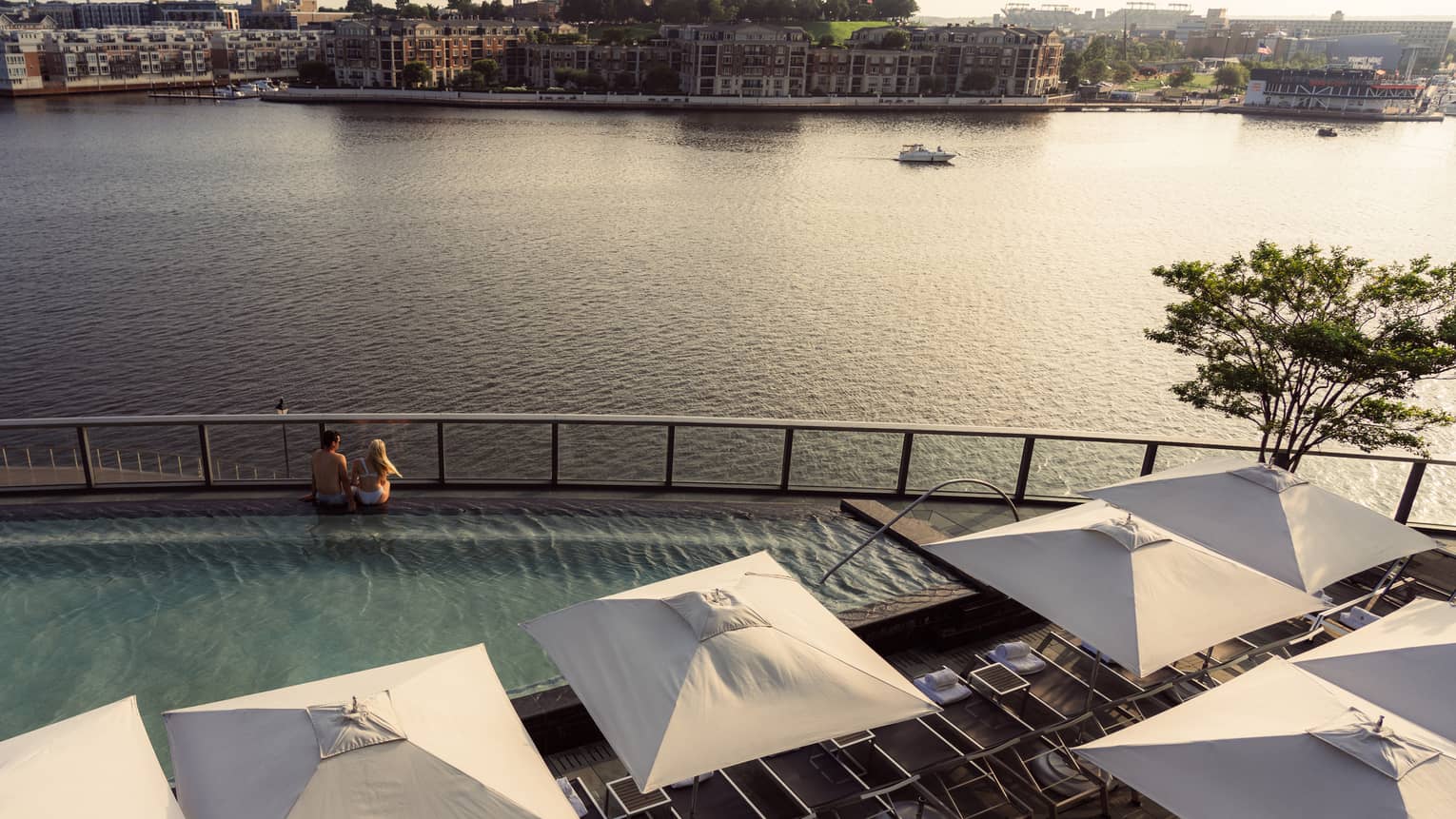 Two people sitting on the edge of a pool overlooking the harbour.