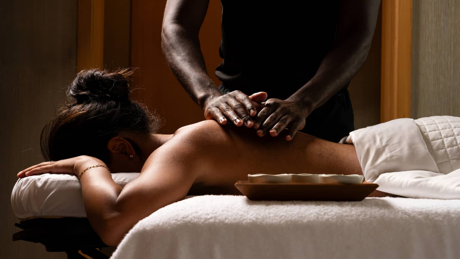 Masseur's hands rub oils on the bare back of a guest lying face down on a massage table