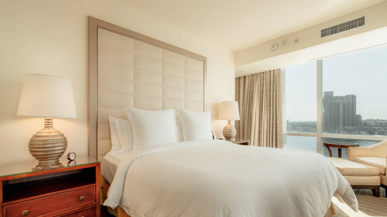 A guest room with floor-to-ceiling windows, two side tables with lamps and a view of the city