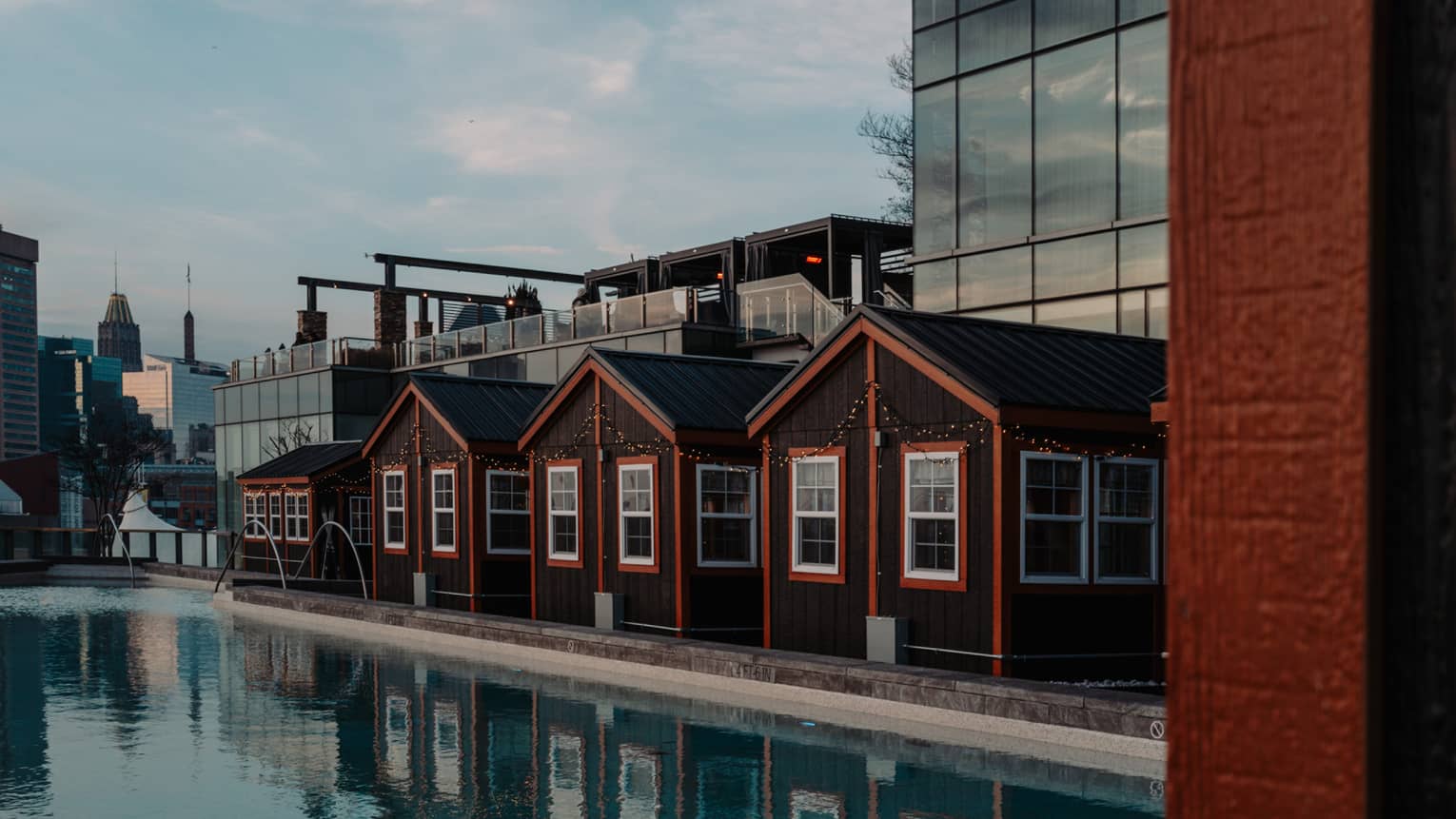 Four cottages with orange trimming beside a pool and city buildings