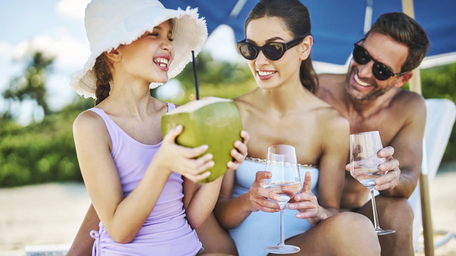 Family wearing swimsuits and sitting in a lounge chair on the beach.