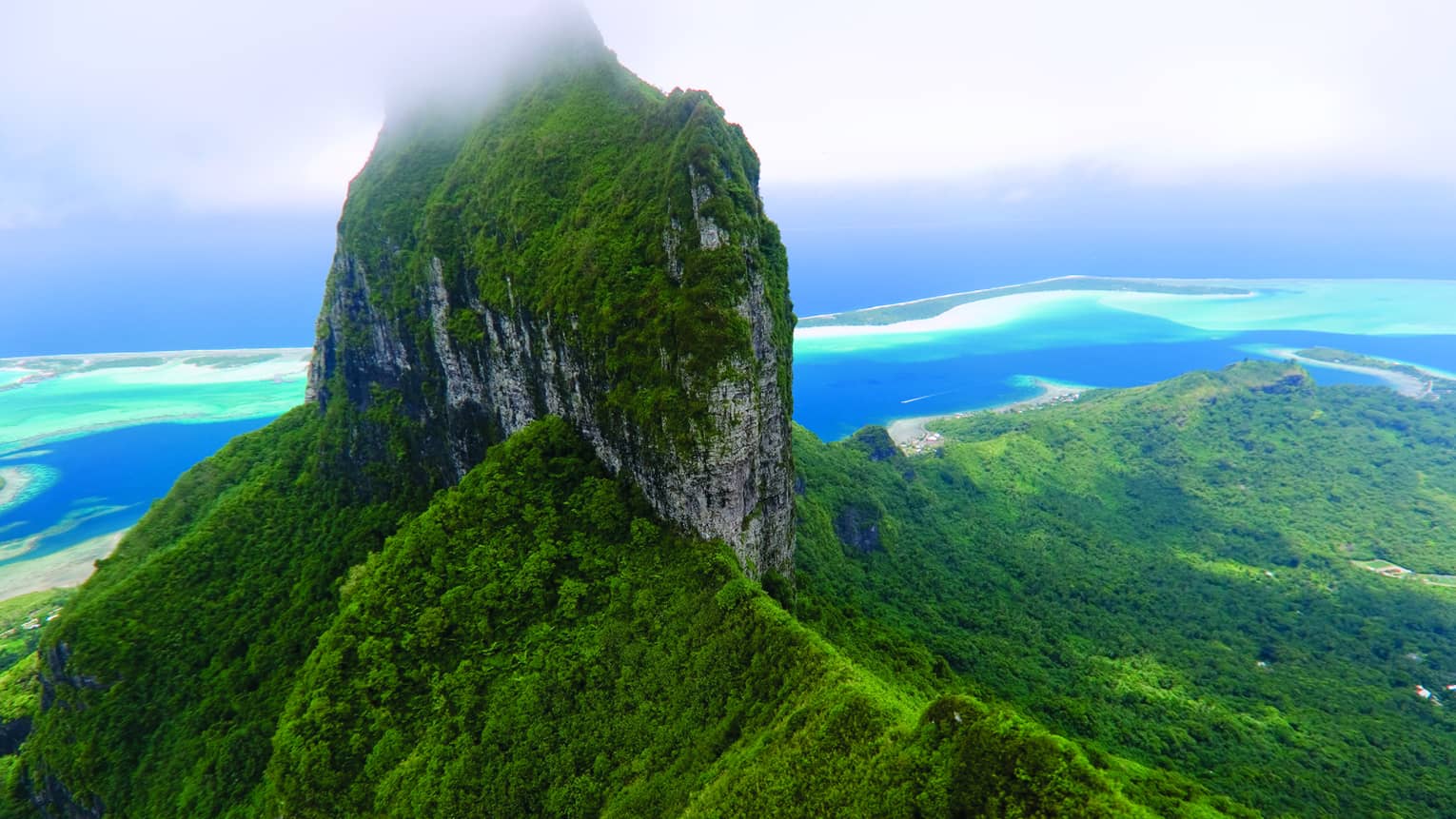 Aerial view over top of tropical Bora Bora mountain, lagoon in background