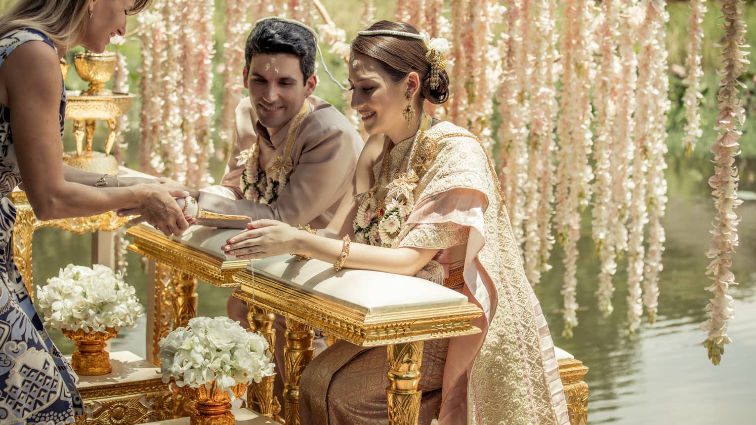 Wedding ceremony, bride and groom kneel at golden altar in front of woman, white flowers