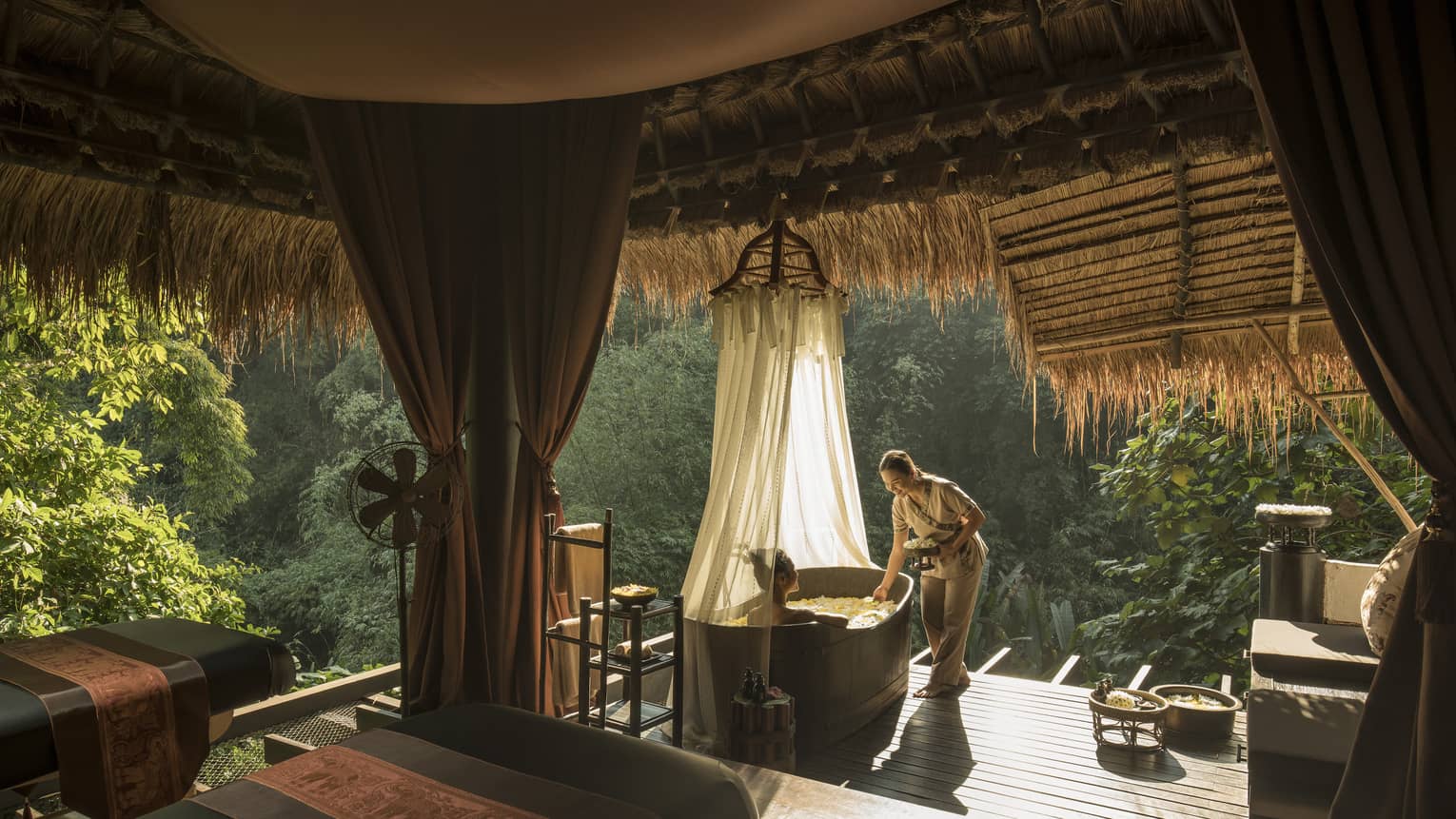 Hotel staff greets woman in spa bath tub in outdoor treatment room