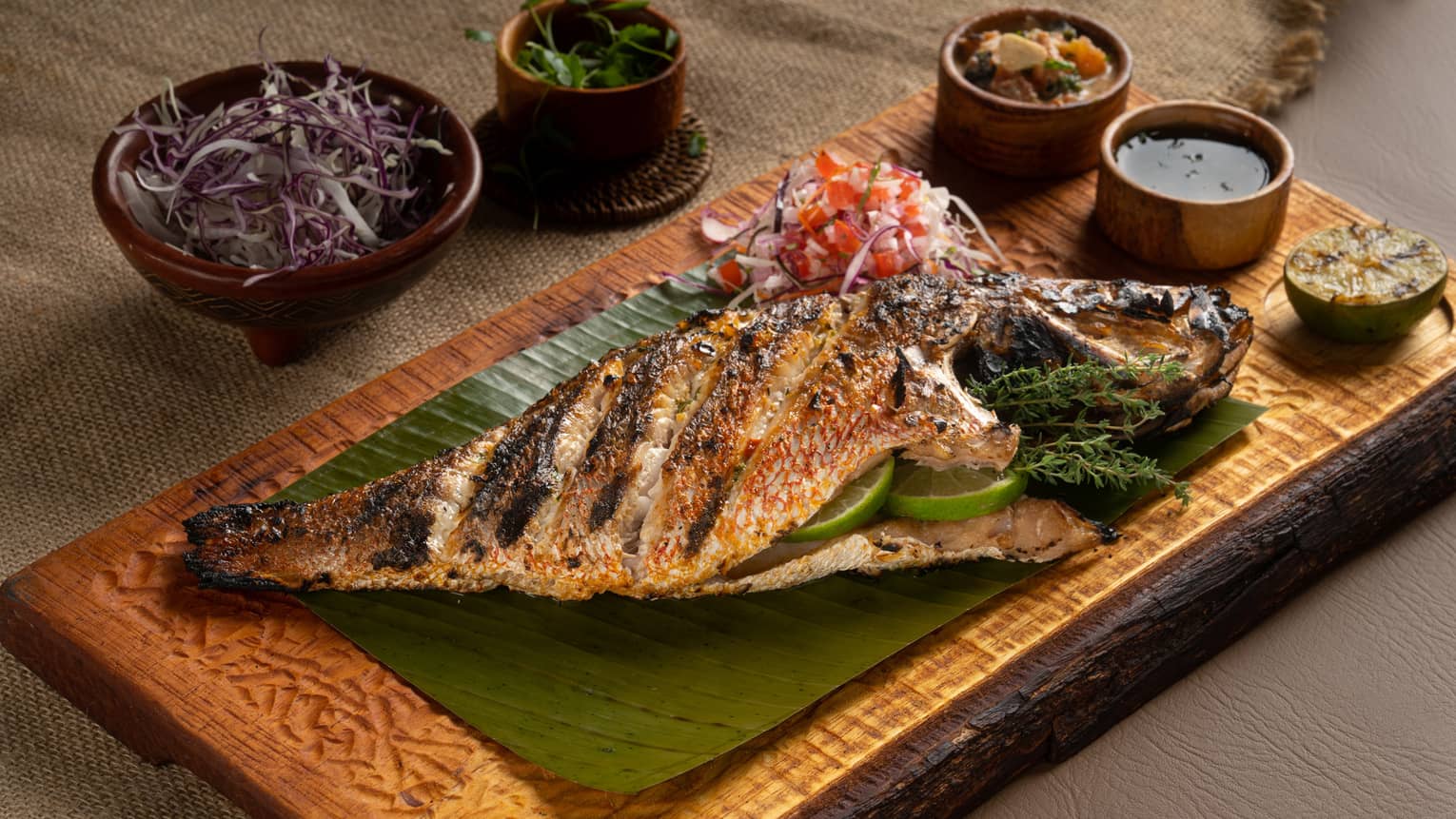 Whole Grilled Snapper served on a wooden plank along with an assortment of condiments and sauces