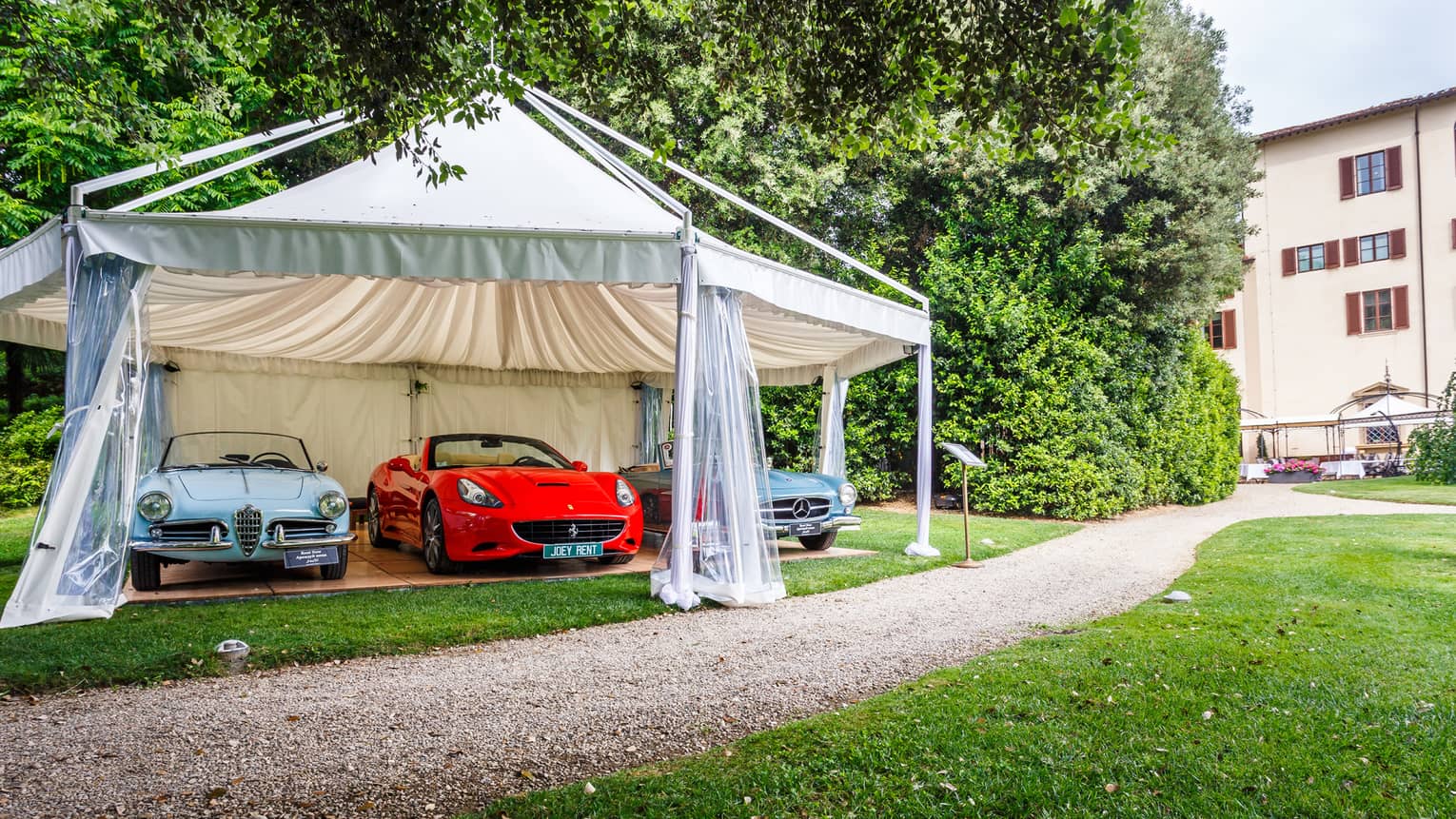 Luxury sports and vintage cars under white canopy tent on driveway