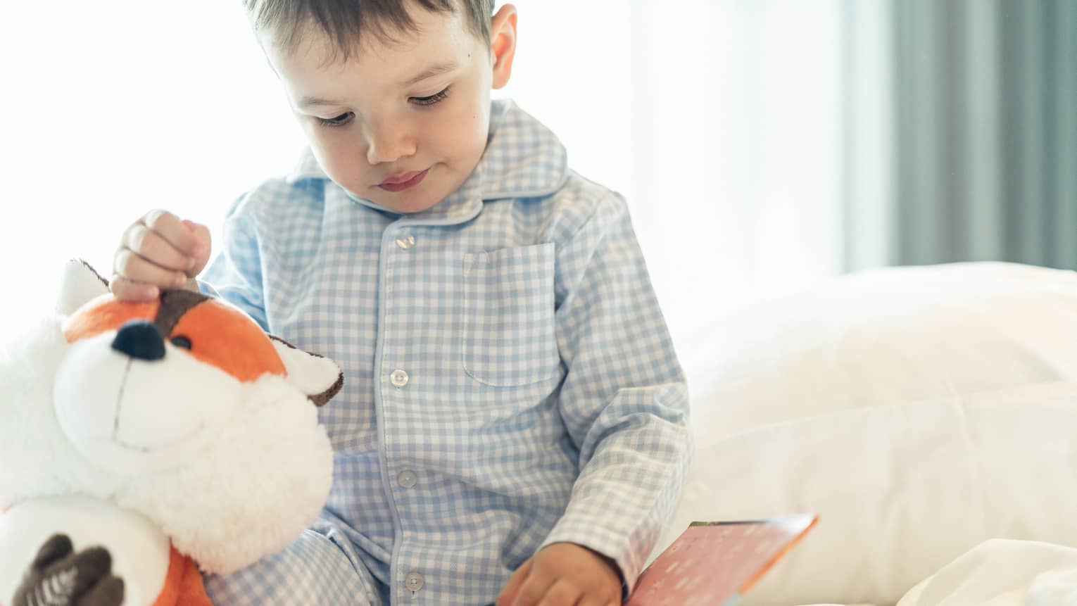 Child holding stuffed animal and reading a book.