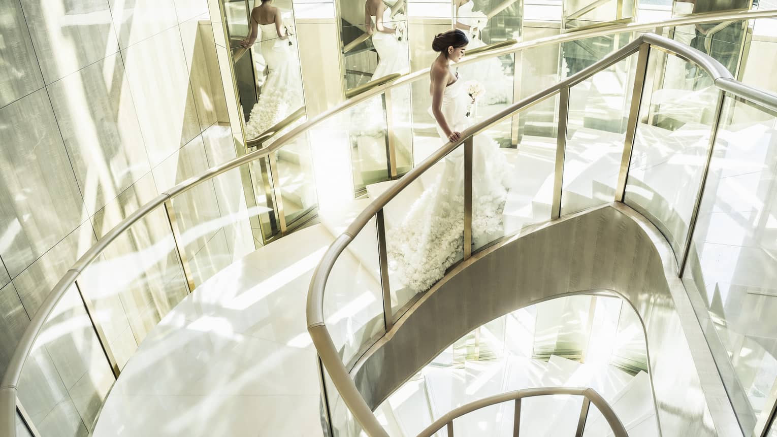 Bride wearing white gown, carrying bouquet walks up glass and marble Grand Staircase