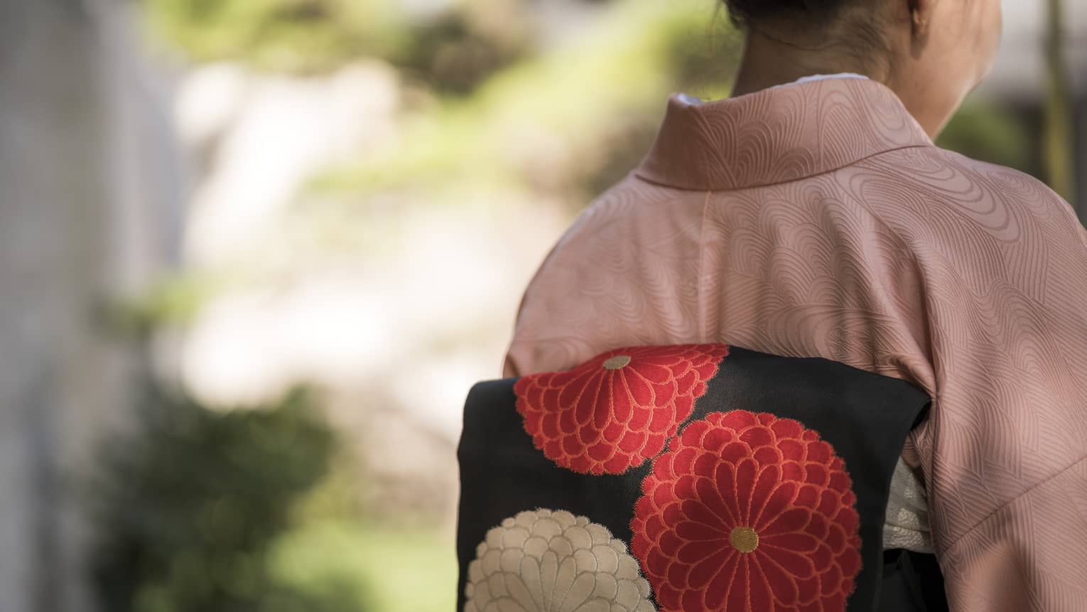 Back view of a person wearing a pink kimono with a black obi featuring red and white floral designs