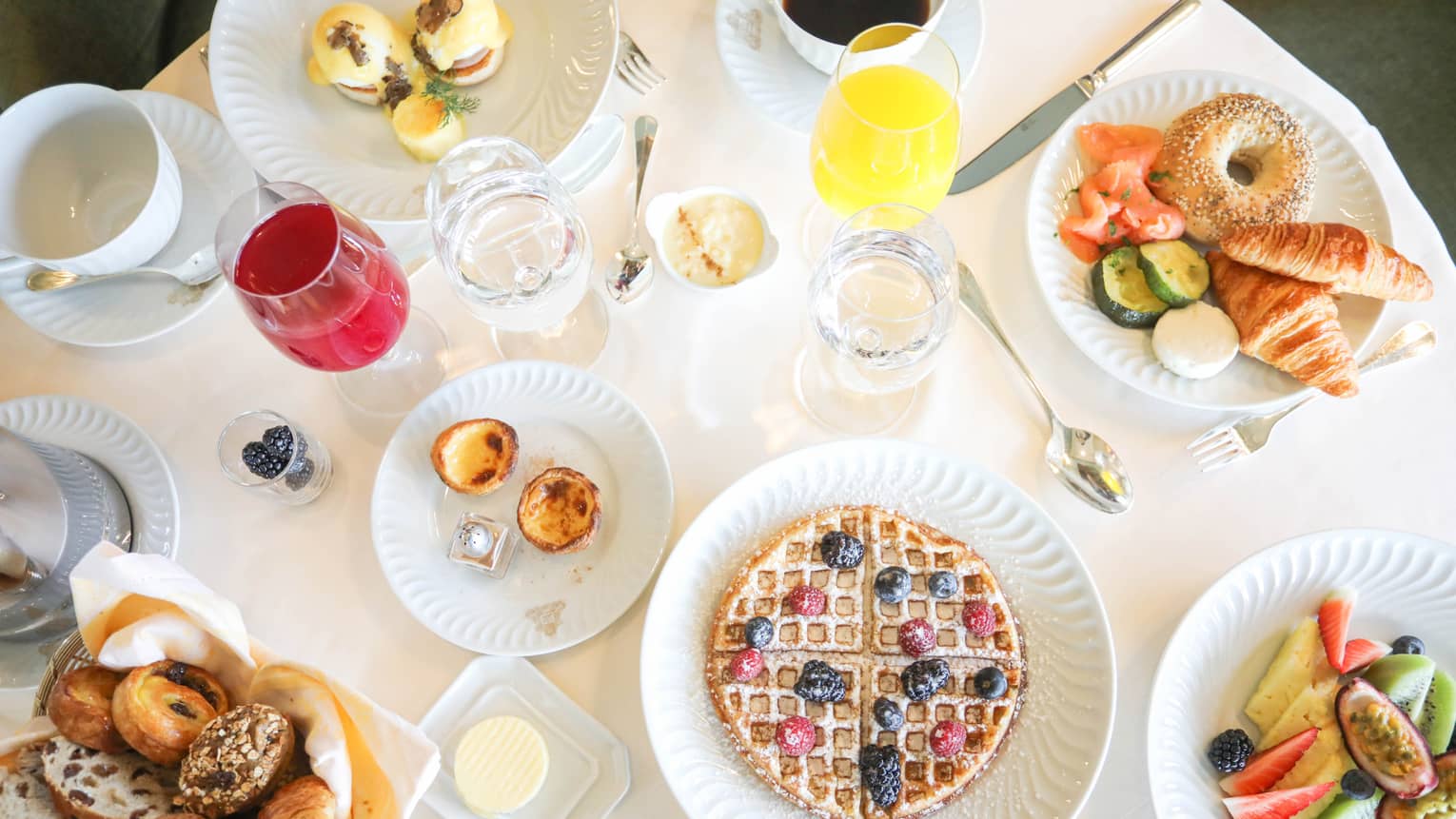 Aerial view of breakfast table with waffles, fresh fruit, pastries and juice in wine glasses