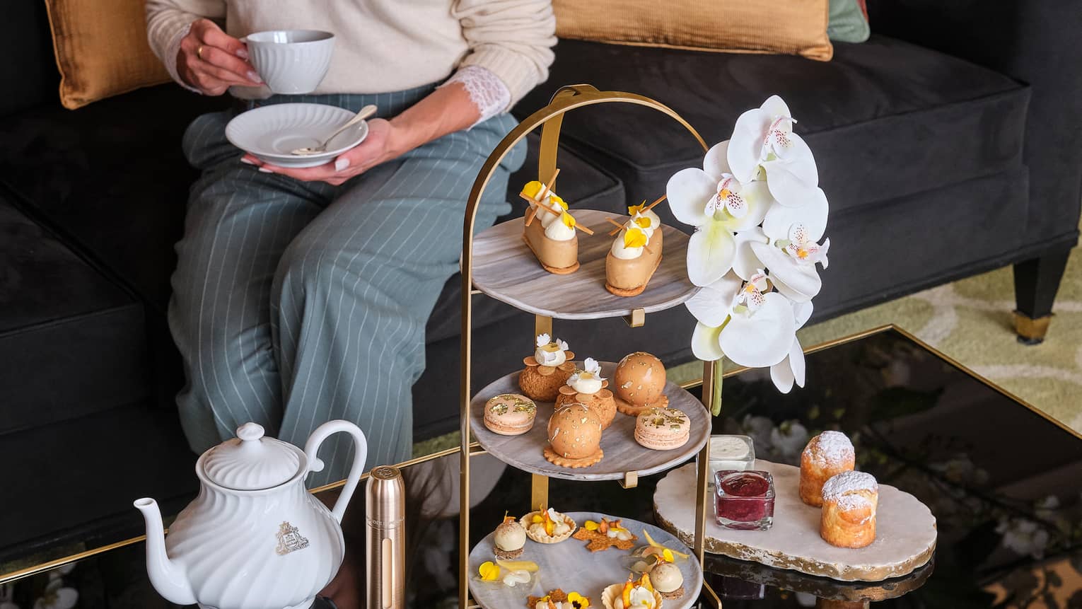 Person seated in front of coffee table topped with afternoon tea stand filled with small bites and treats